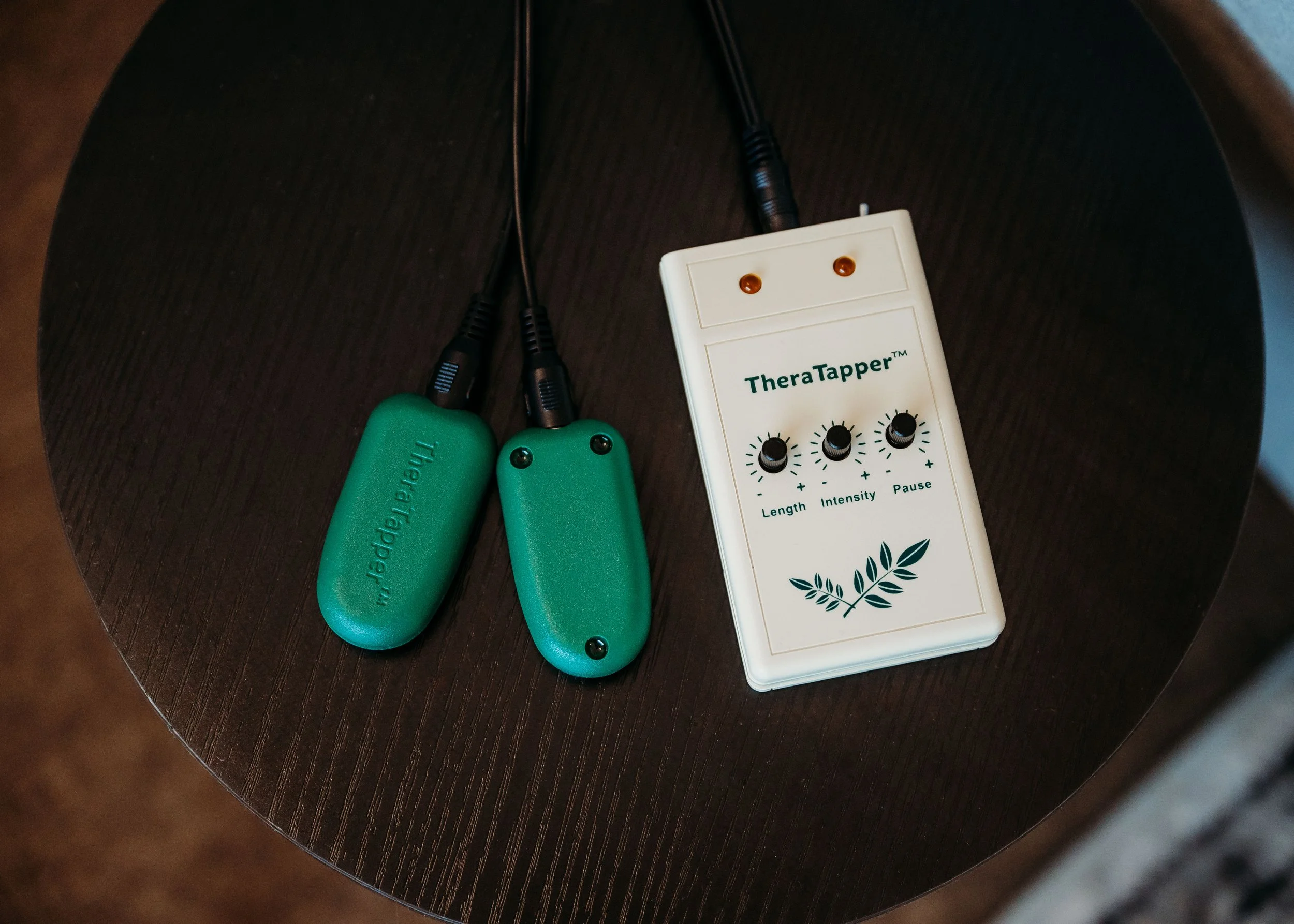 A Theratapper device with controls for length, intensity, and pause, connected to two green massage probes on a dark wooden surface.