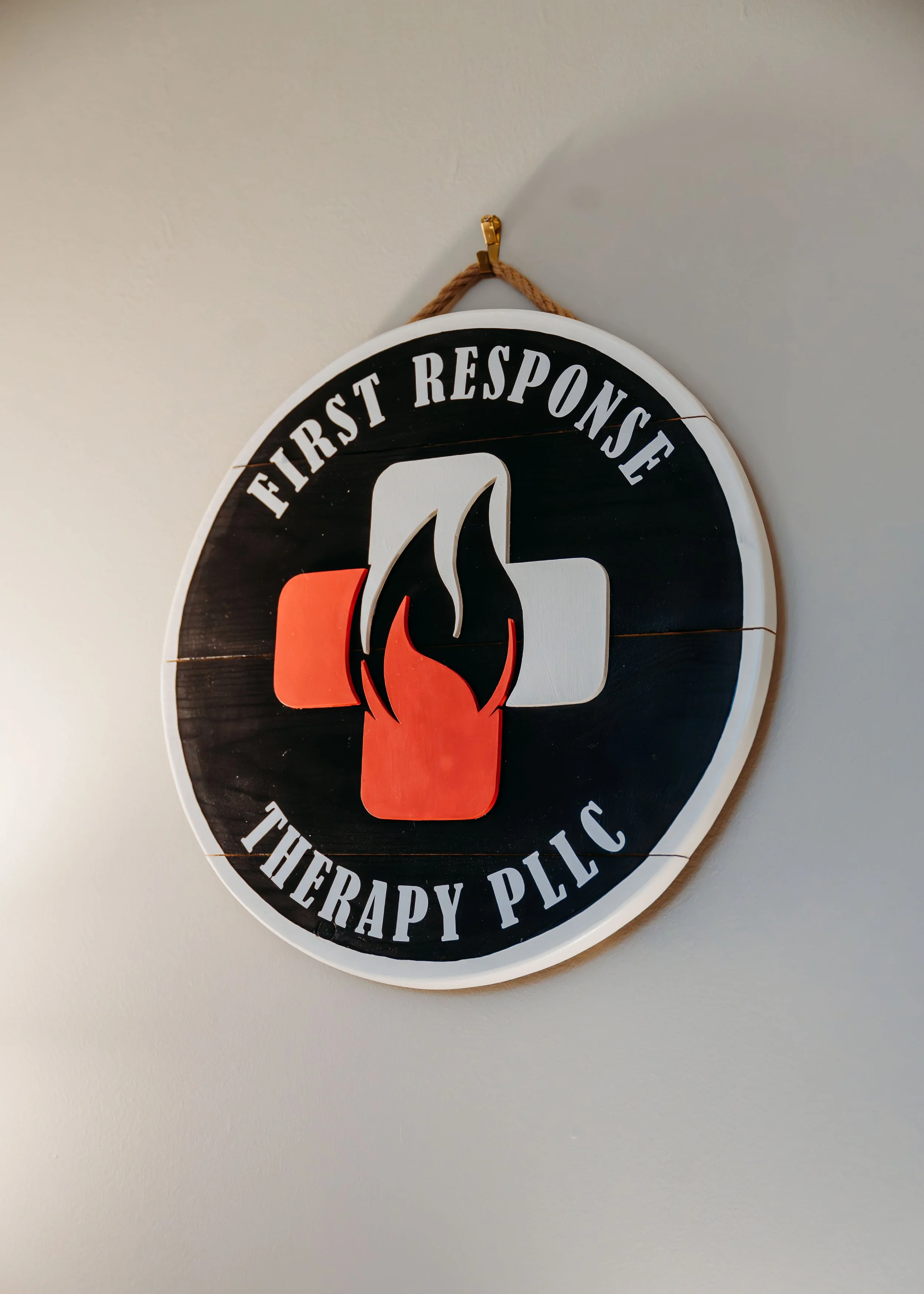Round sign on a wall with the text 'First Response Therapy PLLC' and a graphic of a flame over a medical cross.