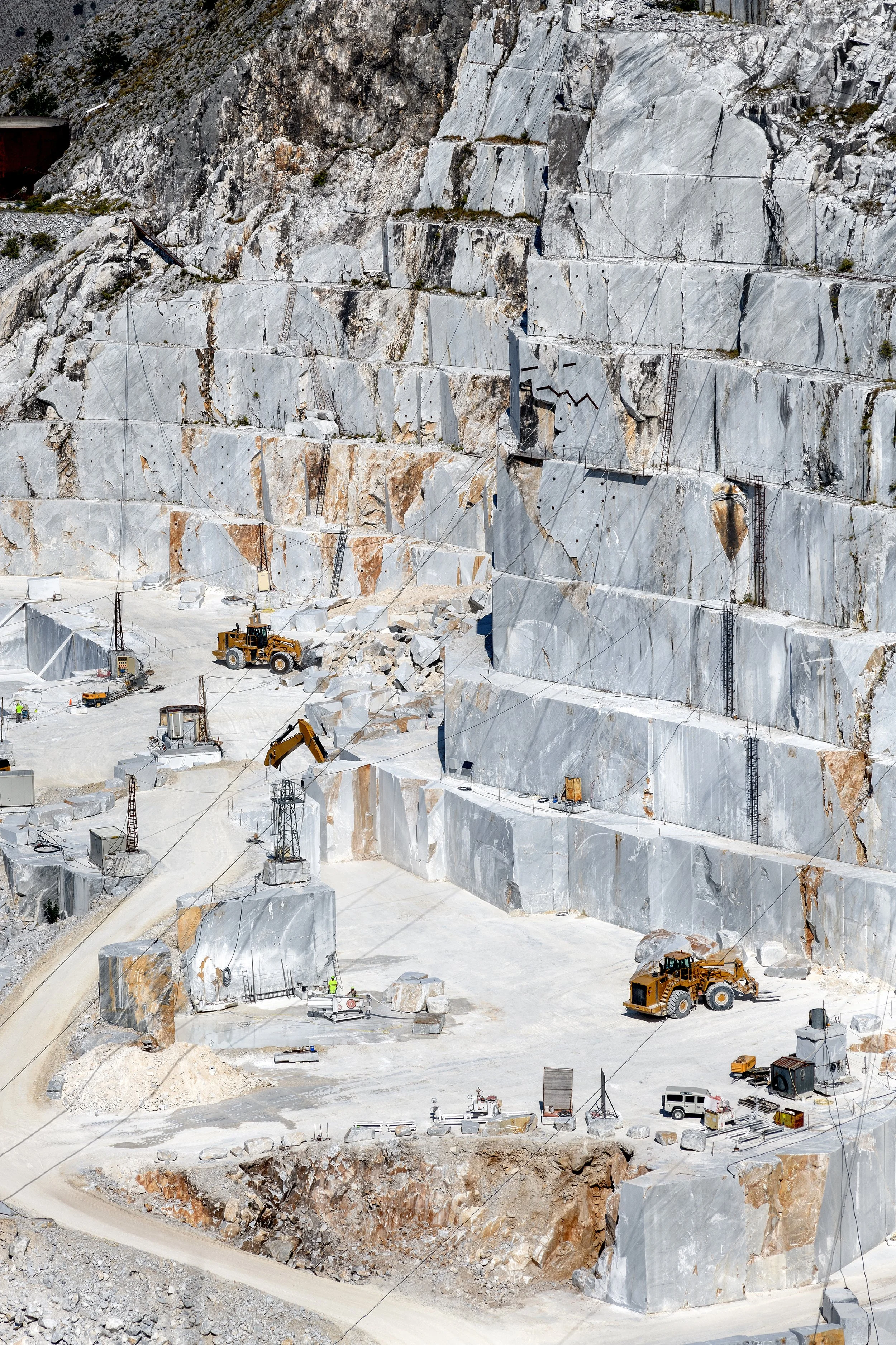 A large marble quarry with heavy machinery, excavators, and trucks working on extracting marble blocks from the mountainside.