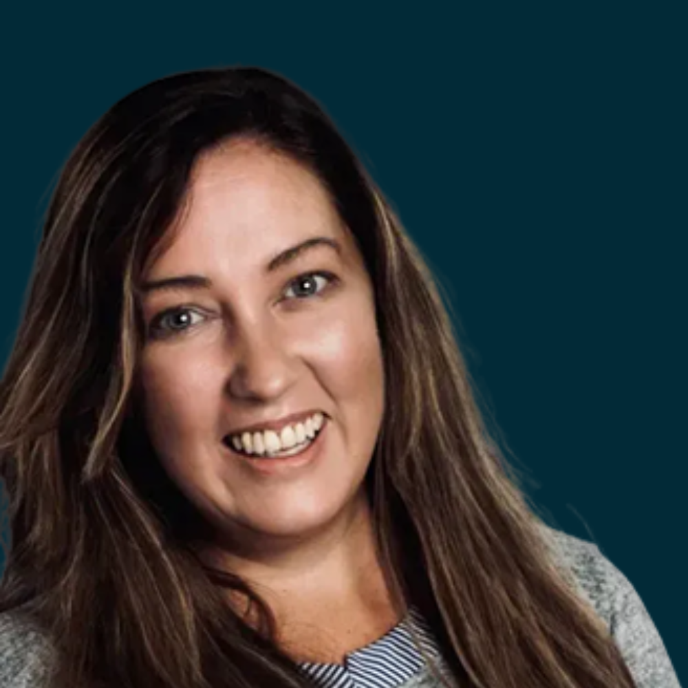 A woman with long brown hair smiling at the camera, wearing a gray sweater over a striped shirt.