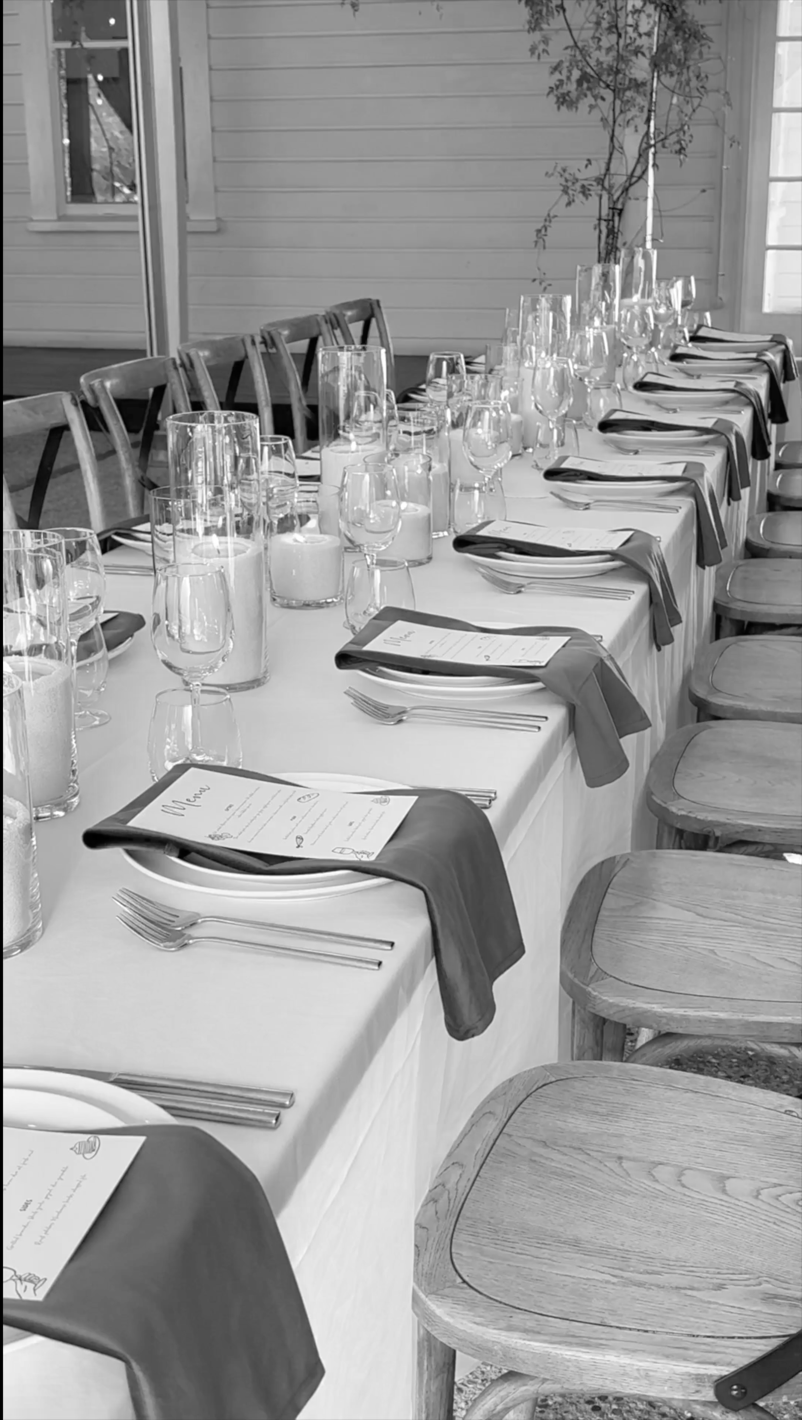 A table set for a formal dinner with plates, silverware, multiple wine glasses, and menus or place cards, arranged neatly with dark cloth napkins.