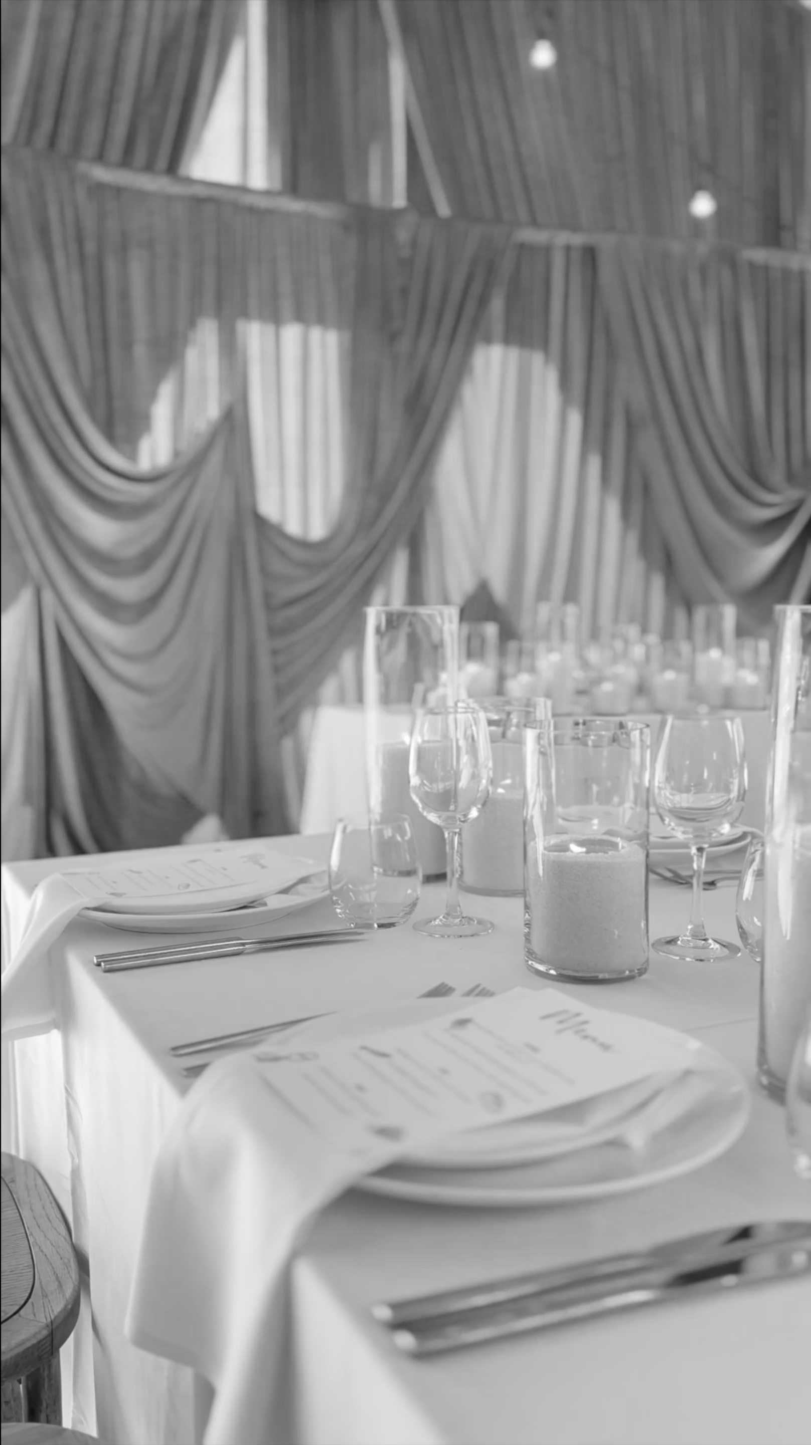 Elegant dining table set with glassware, menus, and utensils in a decorated event venue.