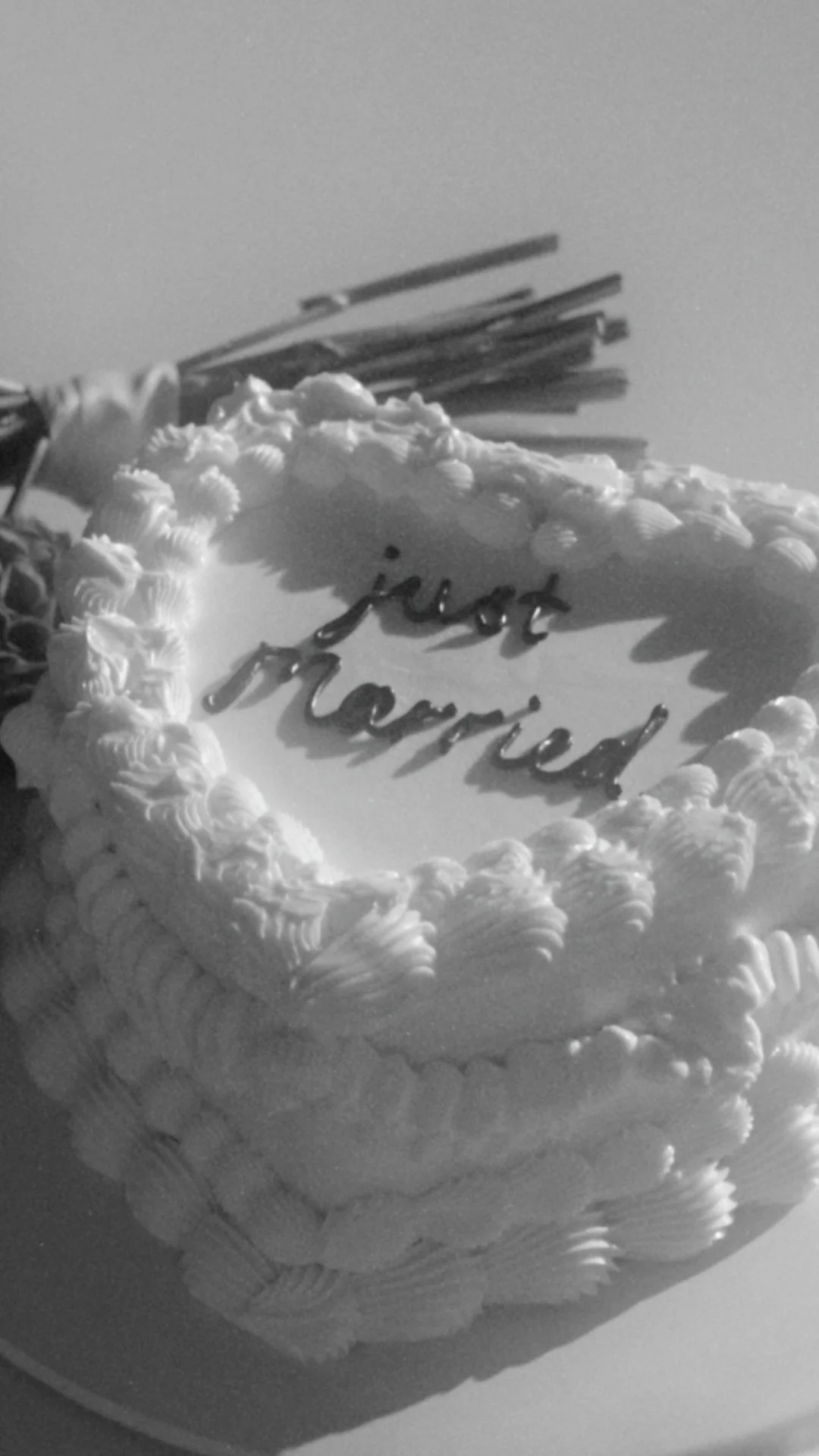 A decorated cake with the words 'Just Married' written on top in metallic letters, surrounded by piped icing and some flowers in the background. Captured by a wedding content creator Queenstown content creators