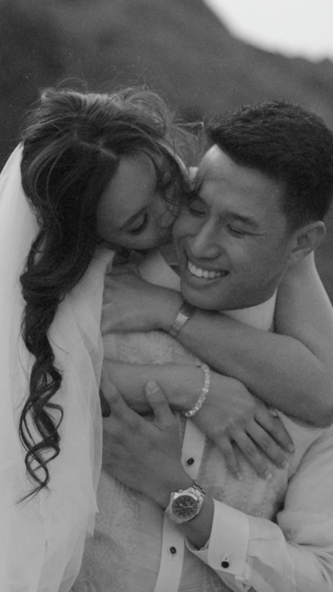 A black-and-white photograph of a couple embracing and smiling, with the woman touching the man's face as they look at each other.