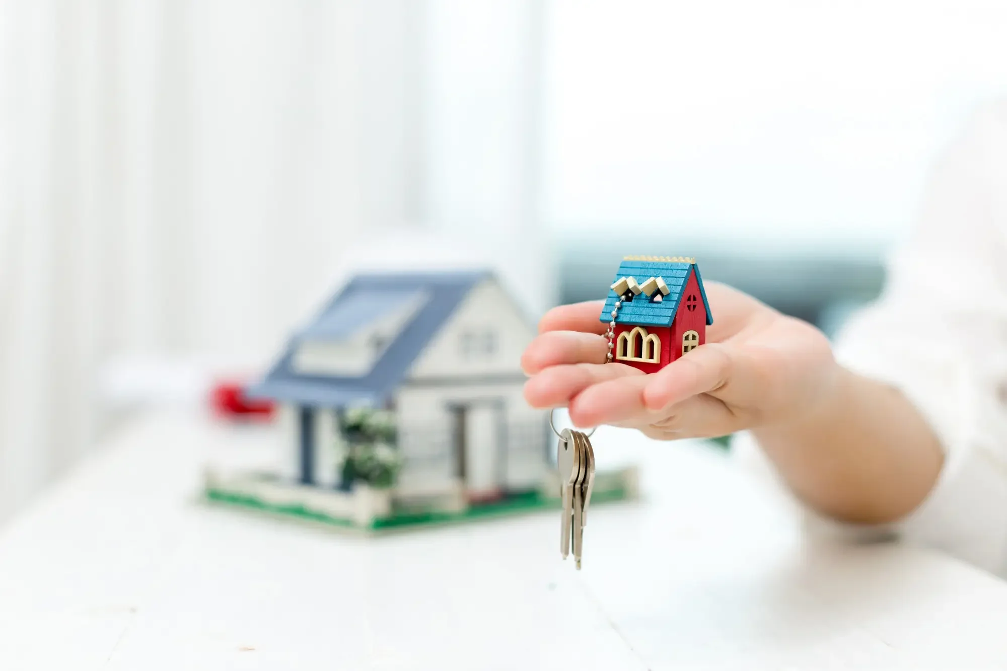 A person holding a mini house keychain and keys to the actual home