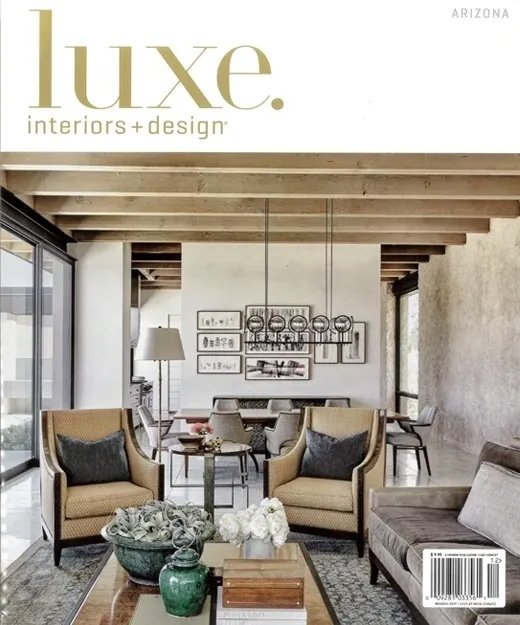Luxe Interiors + Design magazine cover featuring a modern living room with exposed wooden beams, armchairs, a sofa, and decorative plants.