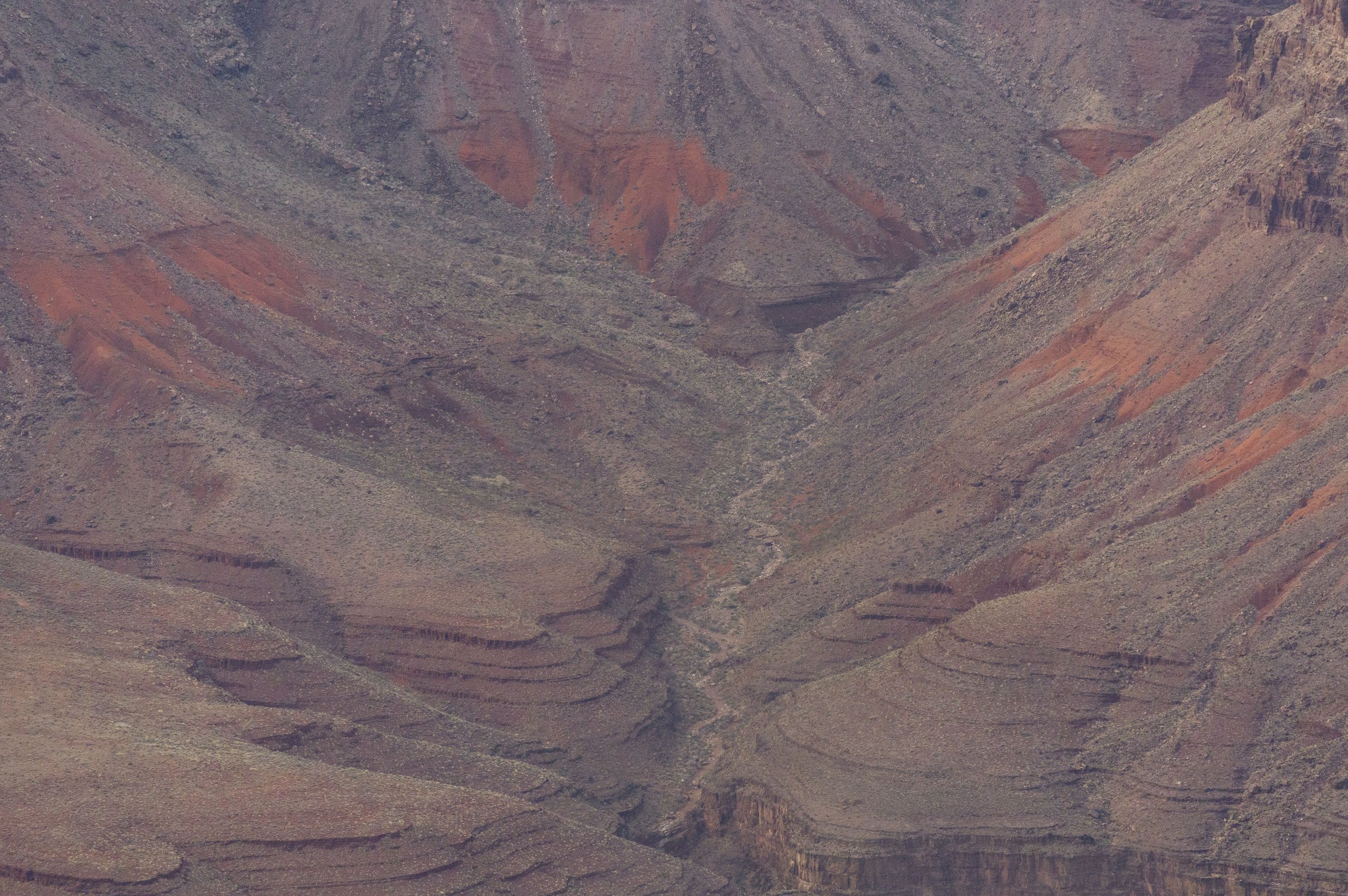 A view of the Grand Canyon showing layered red and brown rock formations, deep valleys, and rugged terrain.