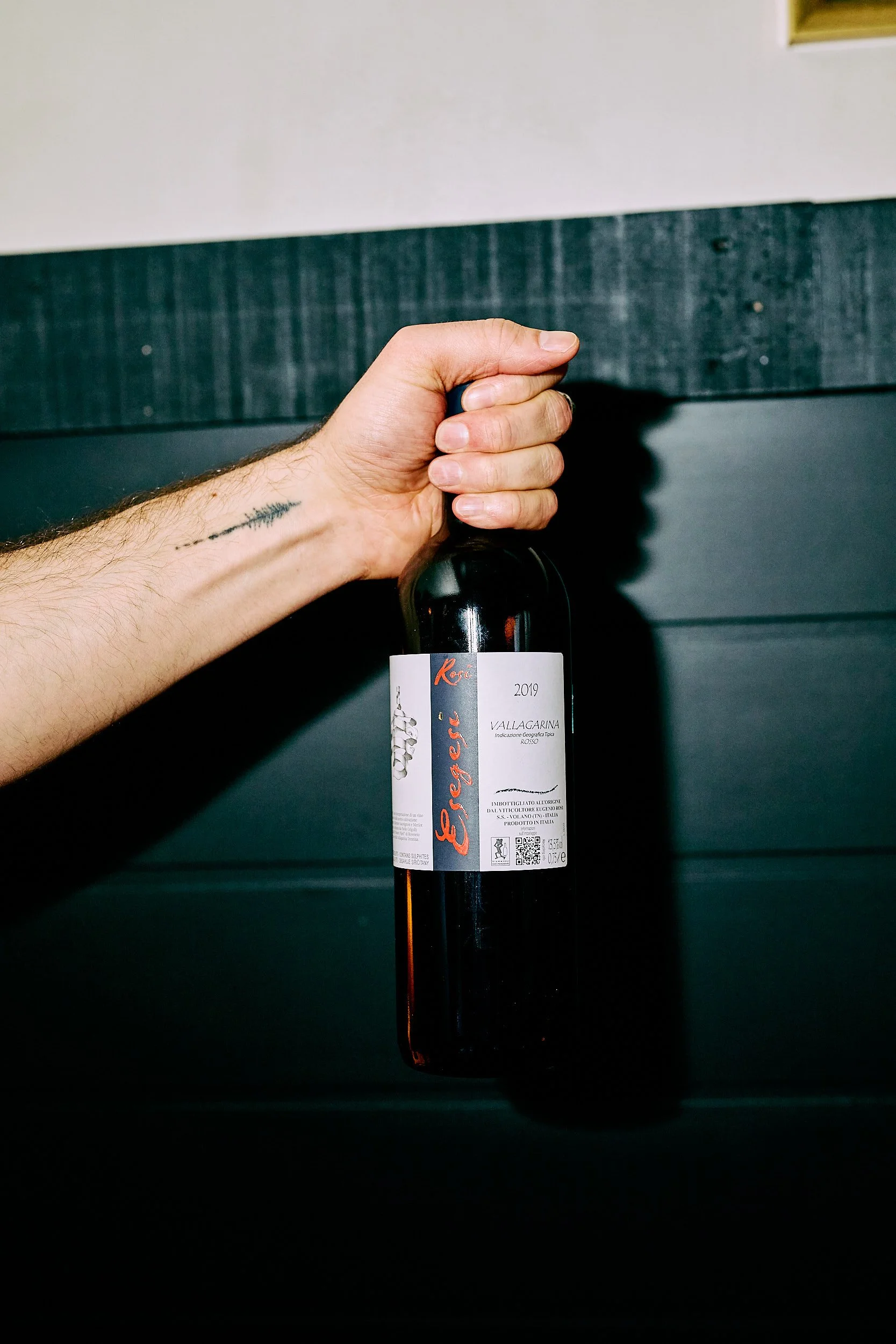 Une main tenant une bouteille de vin rouge portant l'étiquette « Egegeri » sur un fond en bois noir.