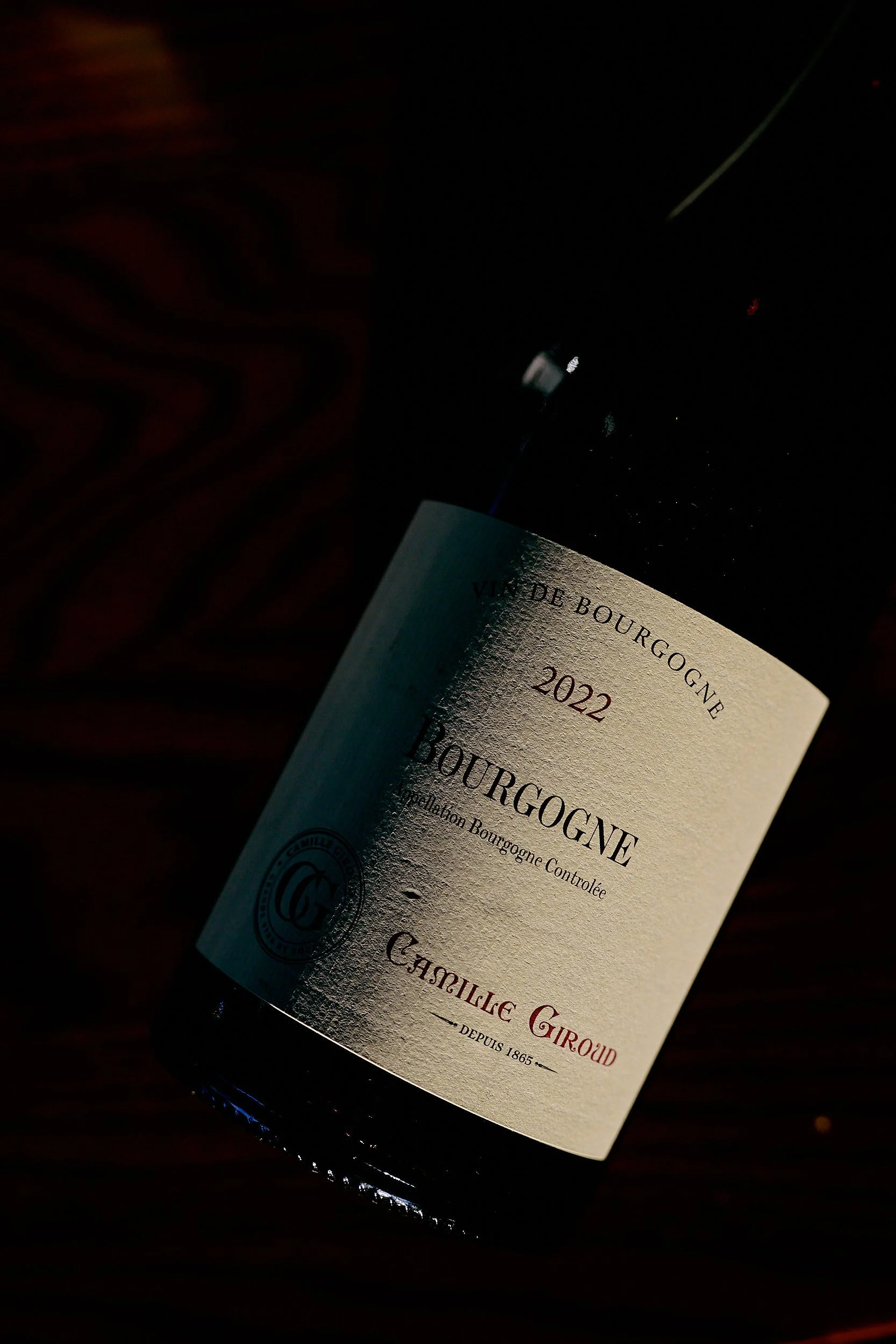 Une bouteille de vin de Bourgogne avec une étiquette crème, posée sur le côté sur un fond sombre.