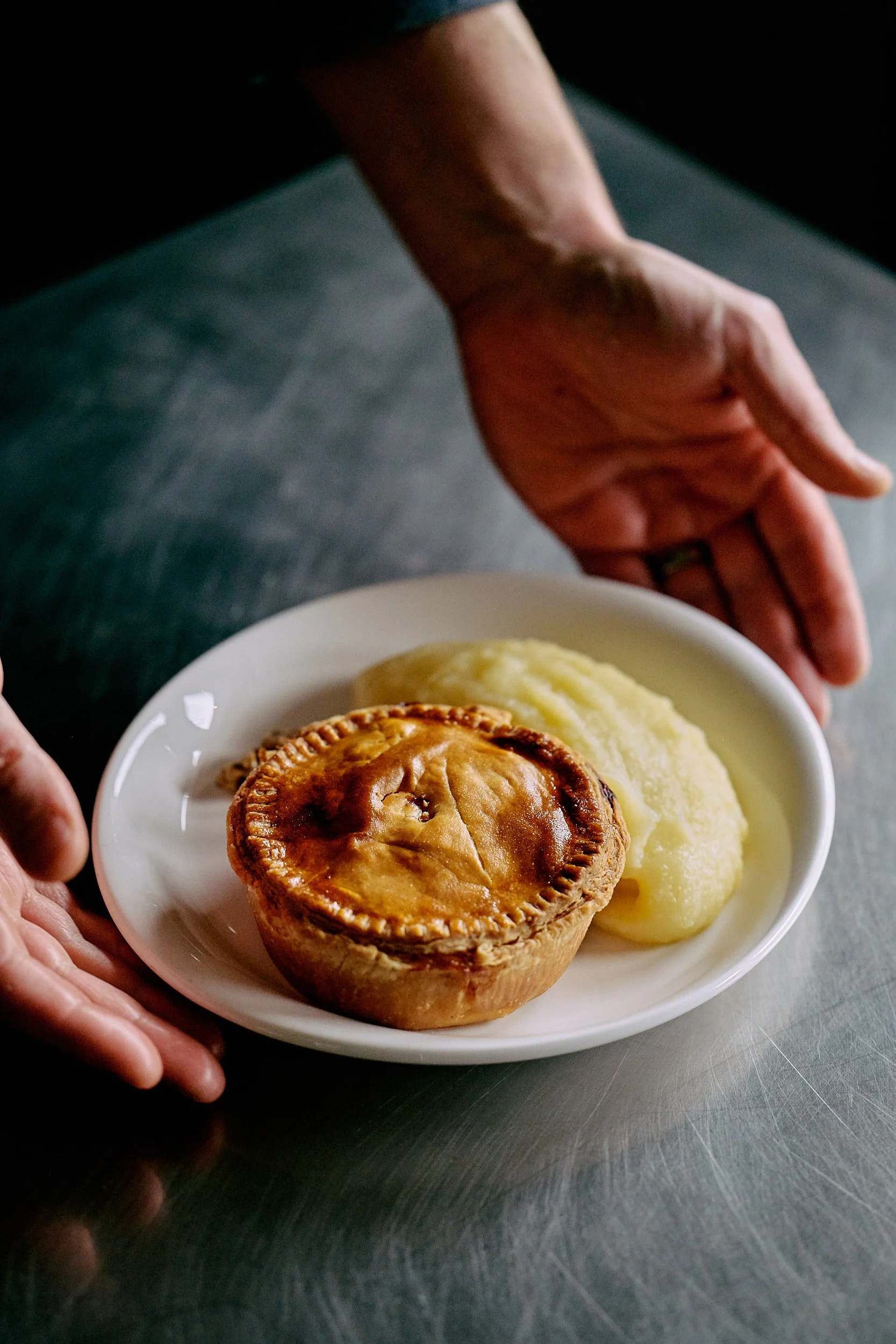 Une personne s'apprête à servir une assiette avec une tourte à la viande et de la purée de pommes de terre.