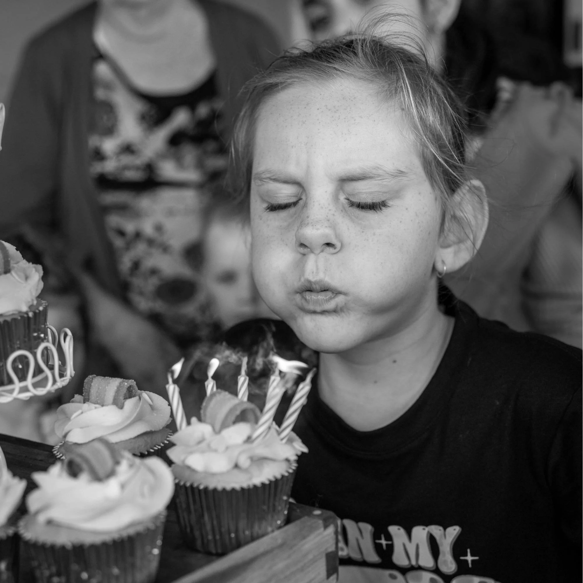 A girl blows out birthday candles on cupcakes