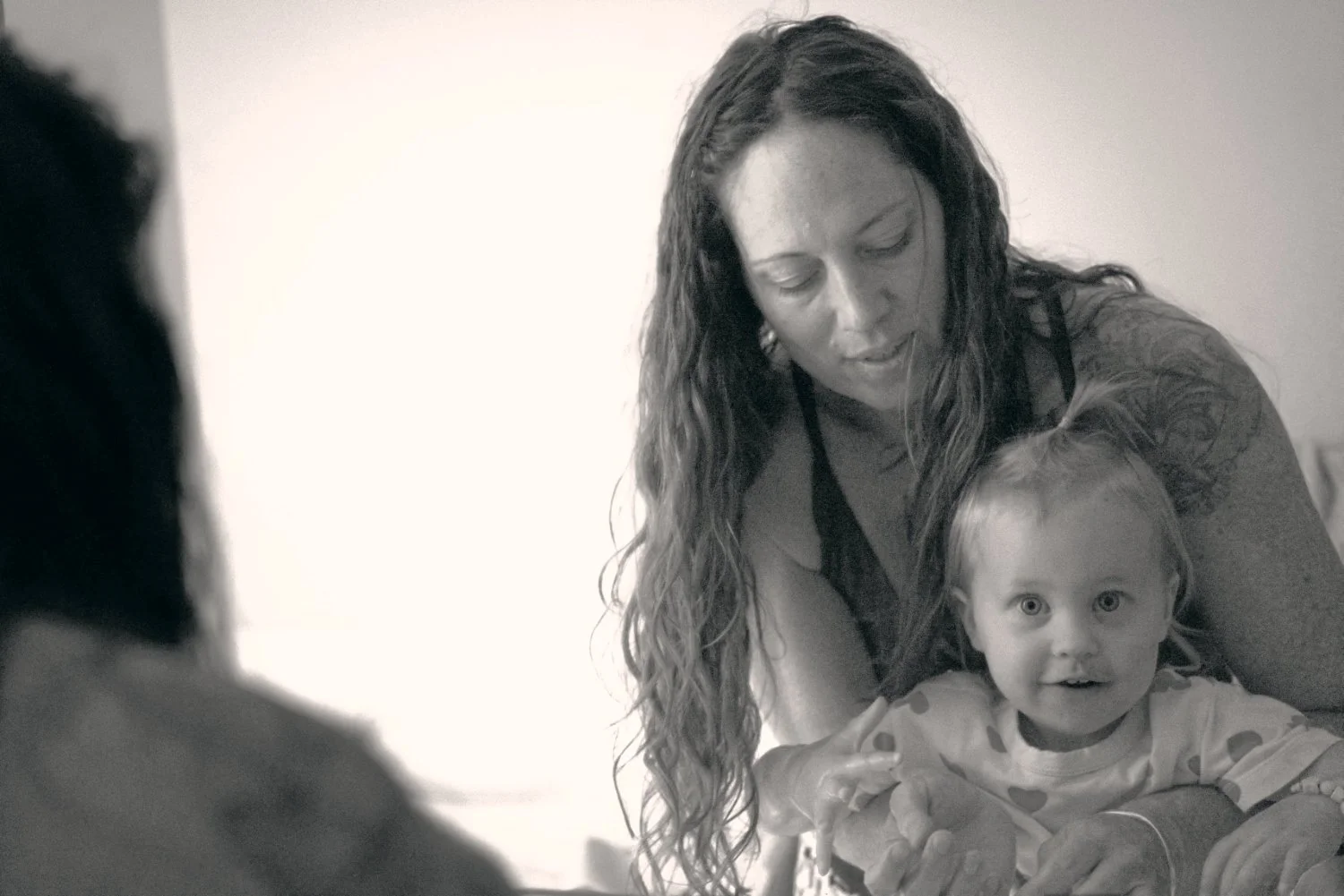 A woman with long curly hair holding a young girl with short hair, both looking towards the camera, in a close-up black and white photo.