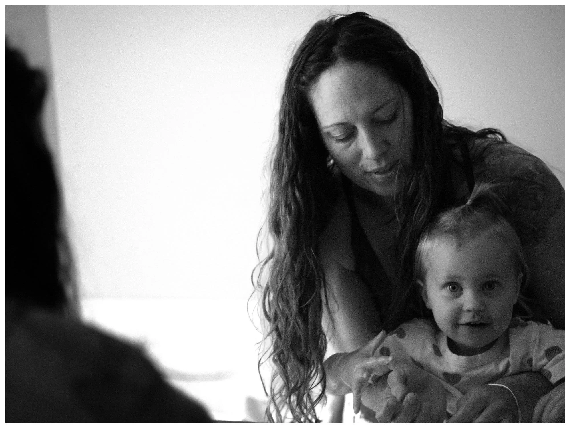 A woman with long curly hair holding a young girl with short hair, both looking towards the camera, in a close-up black and white photo.