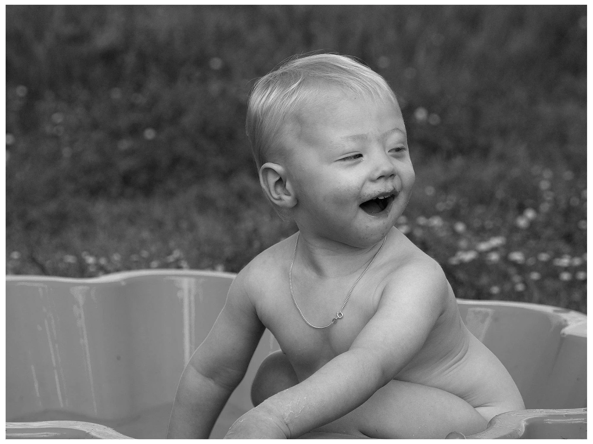 A young child with a joyful expression, sitting in a small children's pool outdoors.