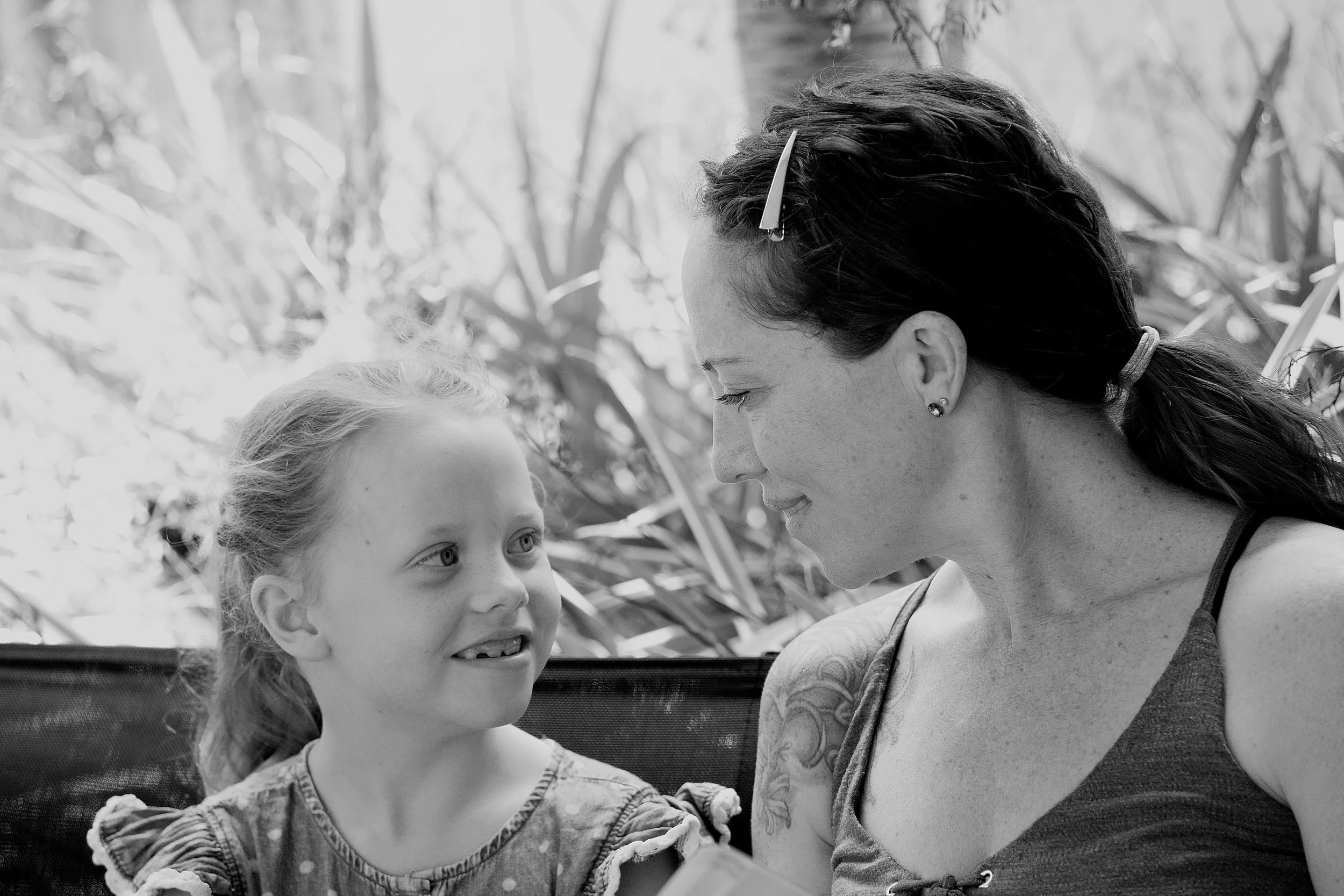 A woman and a young girl sharing a moment outdoors, smiling at each other.