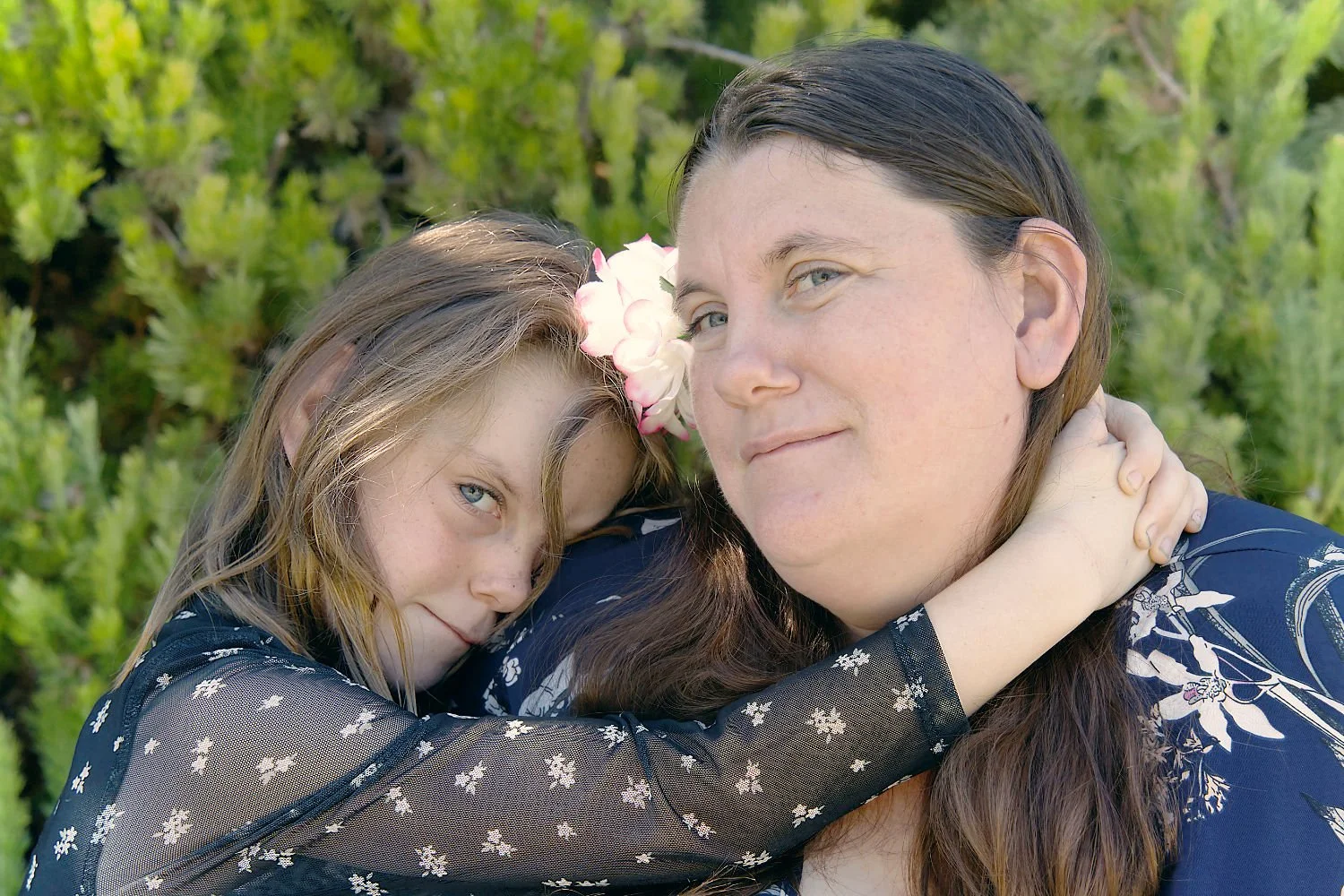 A mother and daughter share a cuddle and smile at the camera