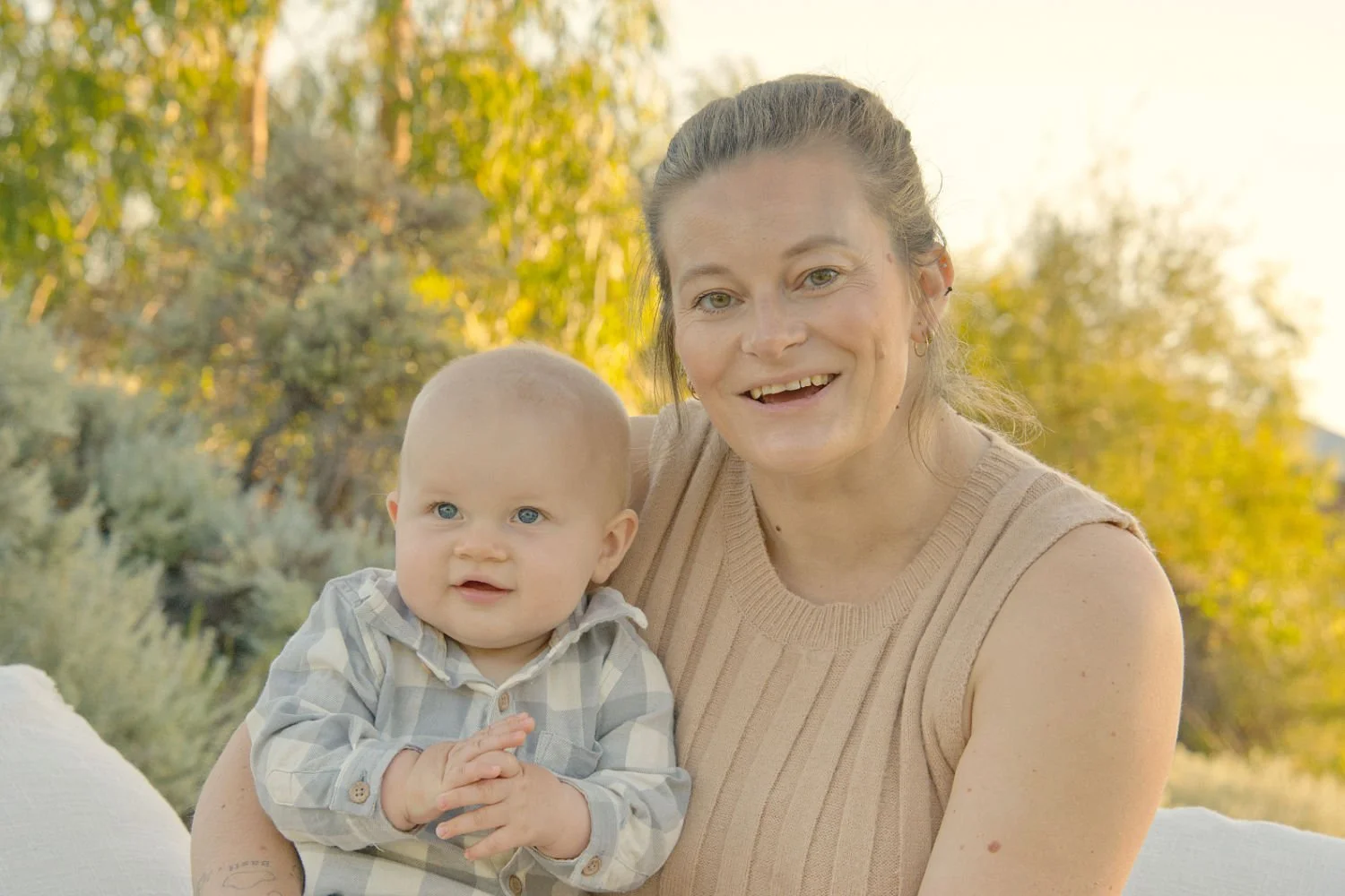 A mother and her baby sit together and smile at the camera