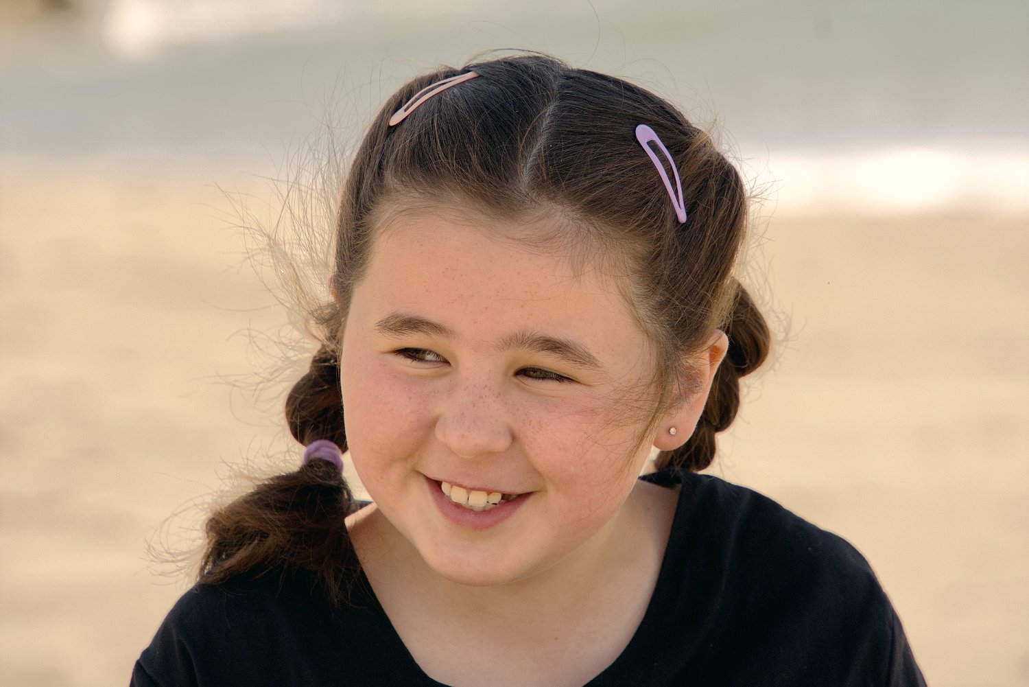 A girl with brown hair in pigtails smiles at the beach