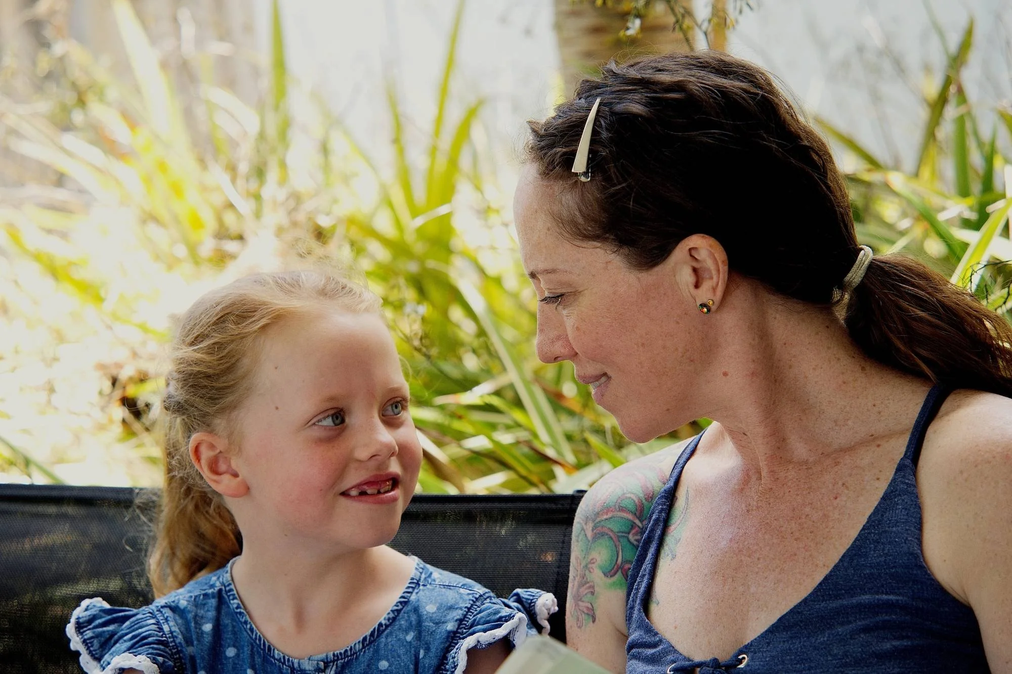 A brunette woman smiles at a blonde girl on a garden bench