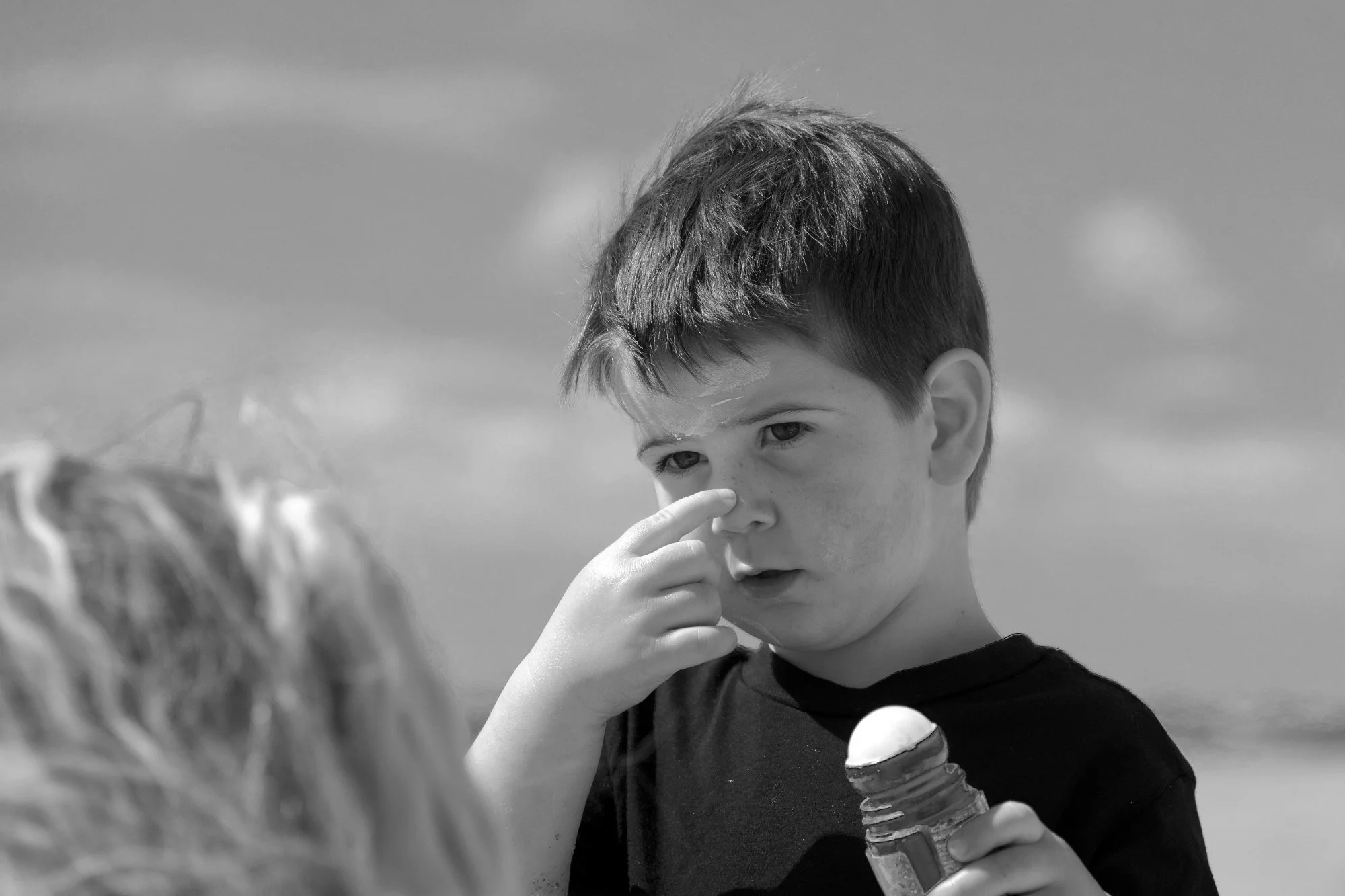 A young boy holds sunscreen and points to his nose