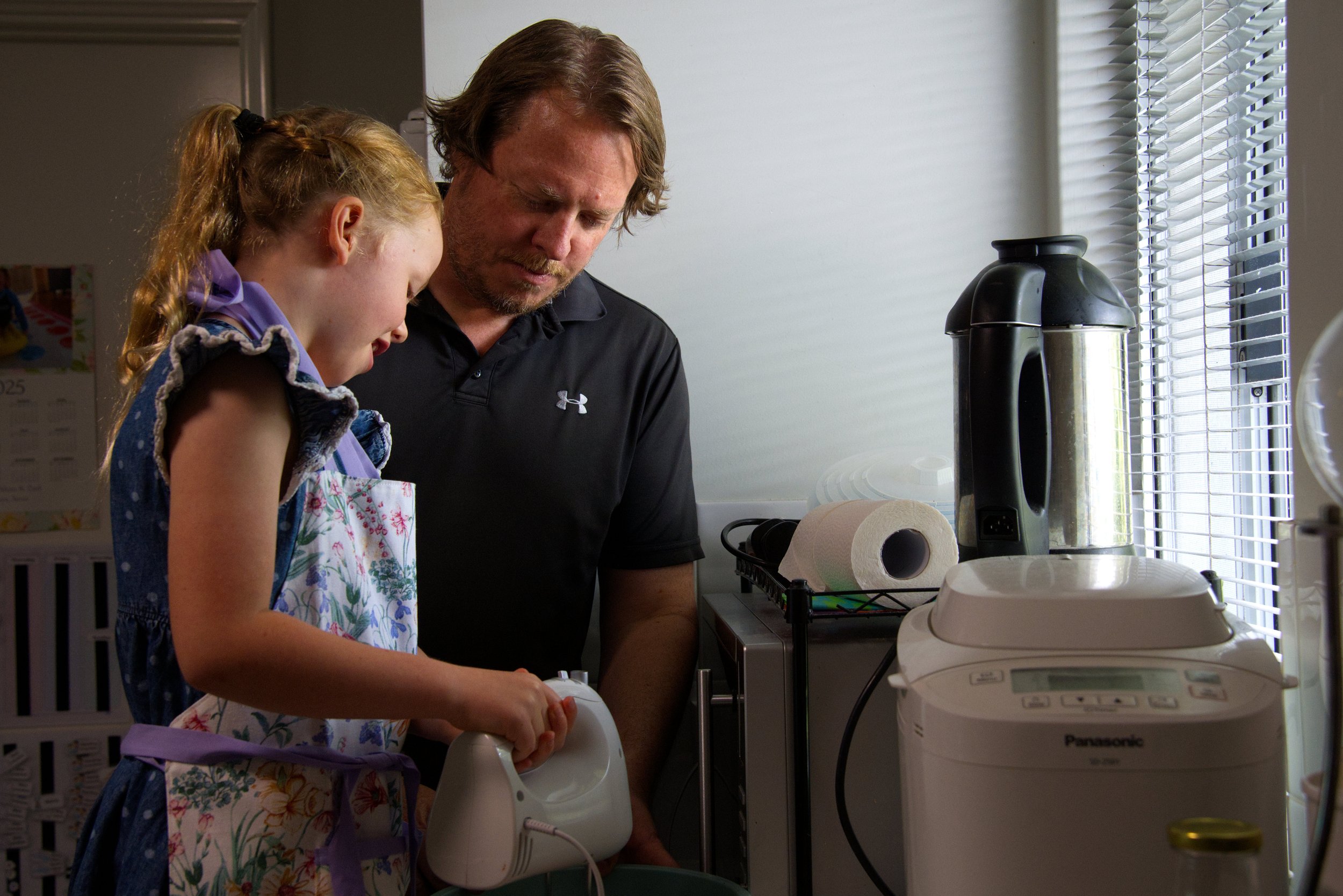 A young girl and a man, likely her father, standing in a kitchen, looking at an electric device the girl is holding.