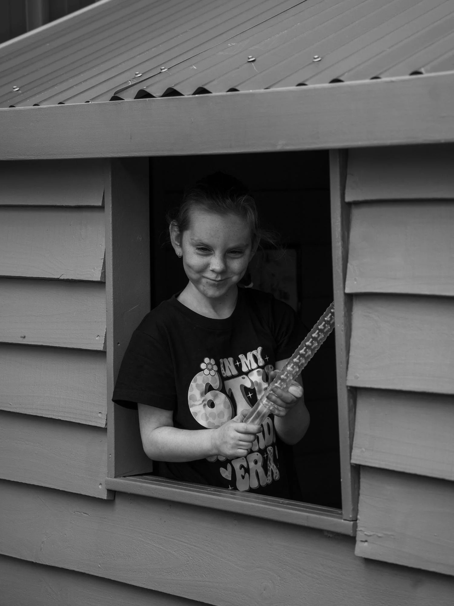 A photograph of a girl in a cubby house playing air guitar and pulling a face