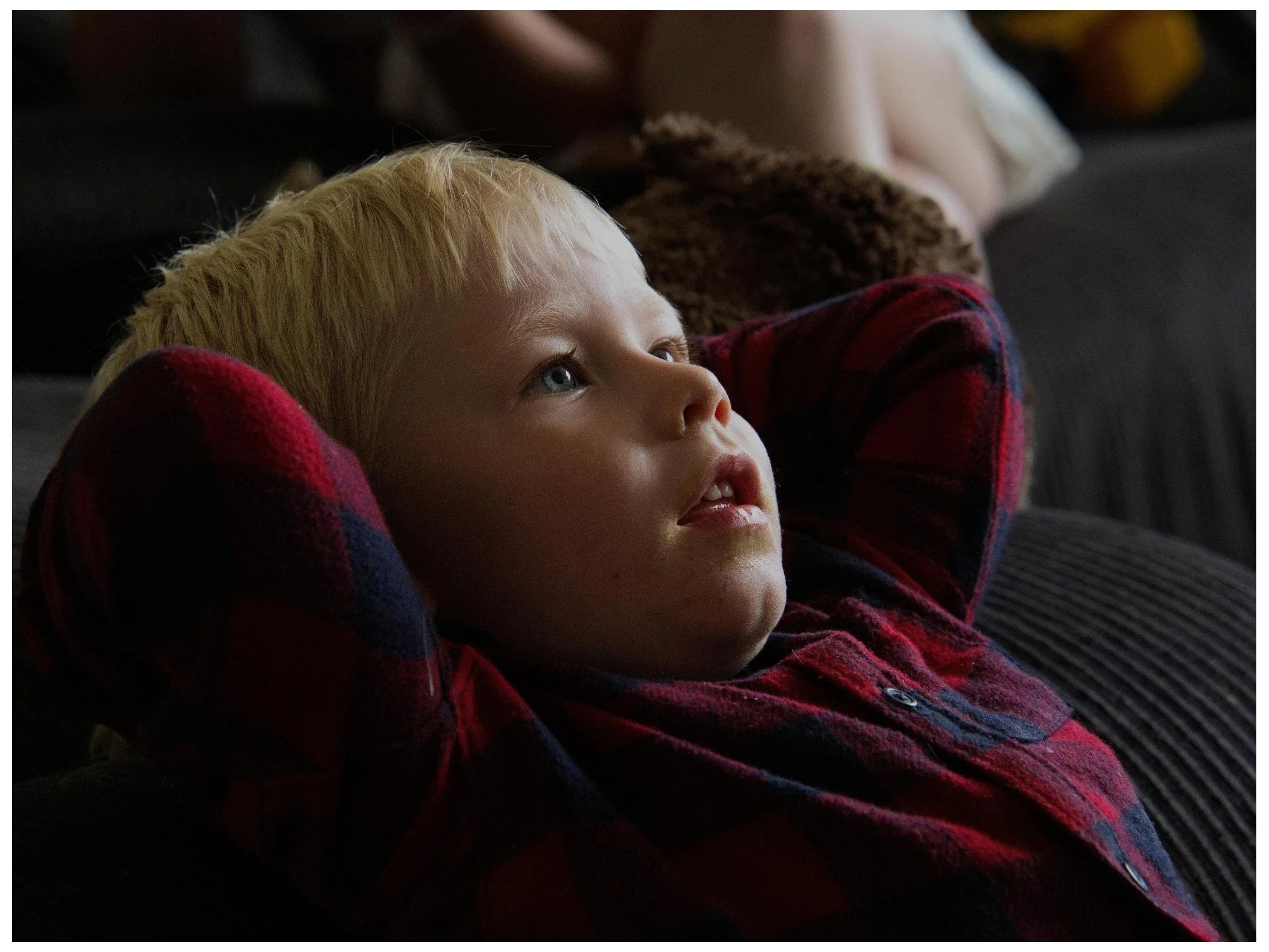Young boy with blonde hair lying on a couch, watching TV.