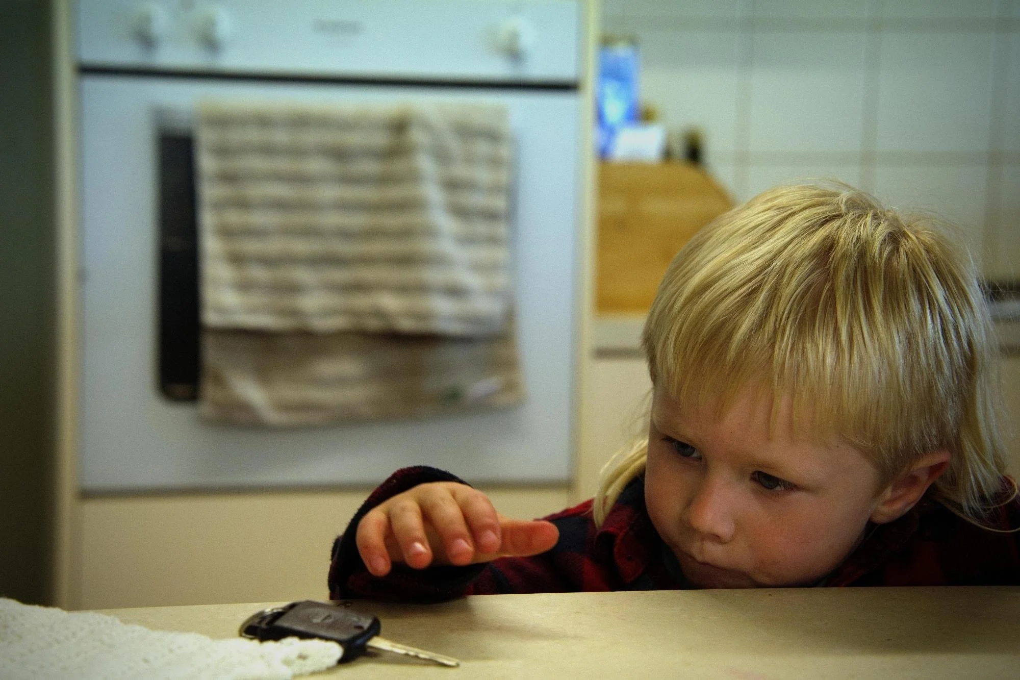 A blonde boy reaches for a set of keys on the kitchen counter