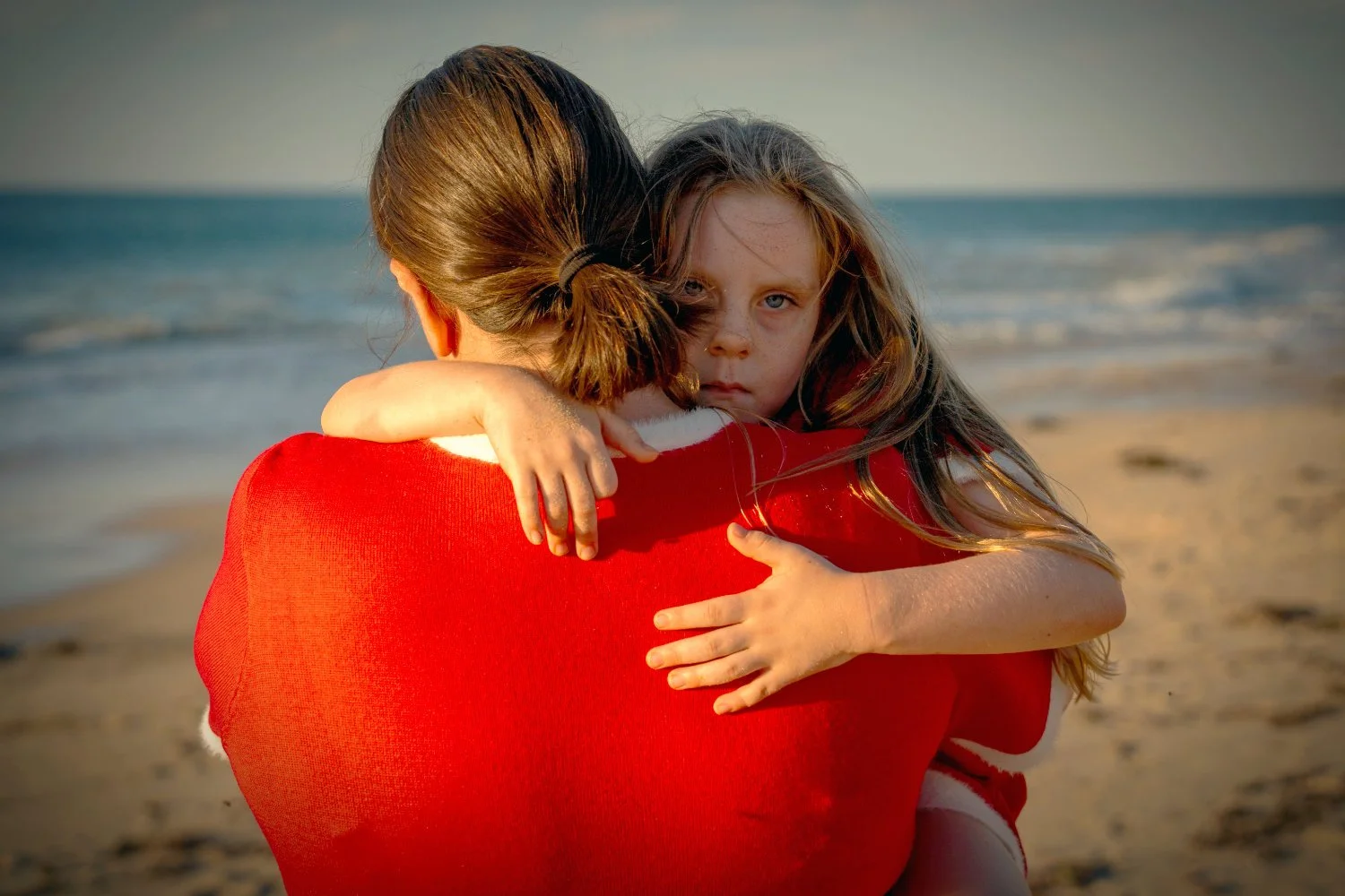 A girl peers over her mothers shoulder at a beach in Halls Head