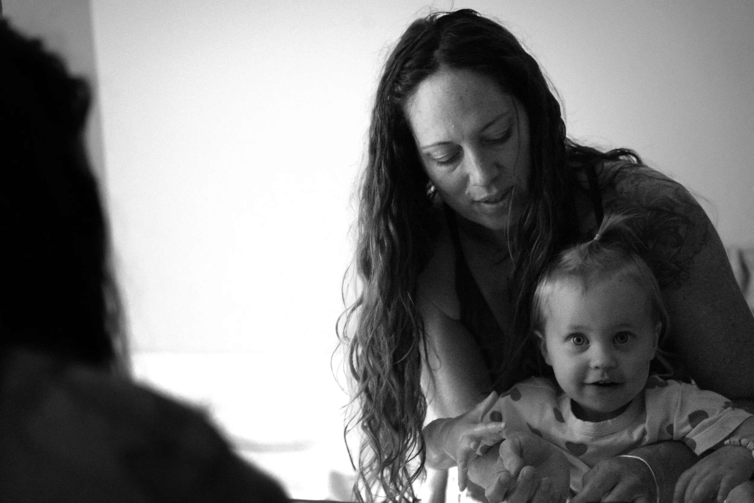 A woman with long wavy hair holding a young girl with light-colored hair and bright eyes, both looking towards the camera, in a black-and-white photo.