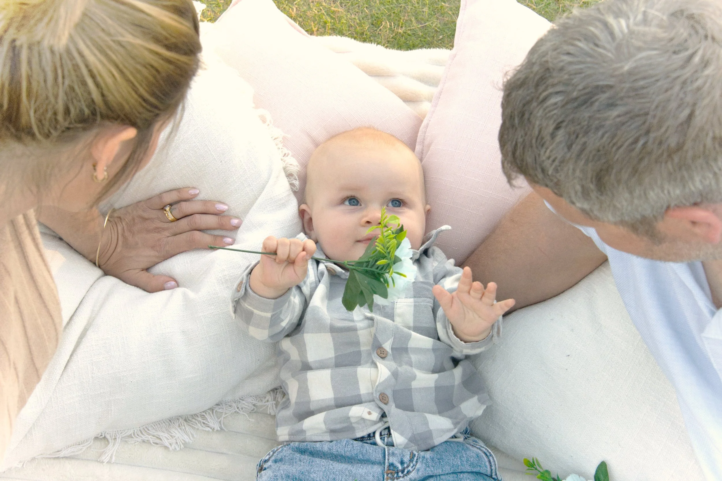A baby lies on a white blanket and smiles up at mum and dad in a photography session in mandurah