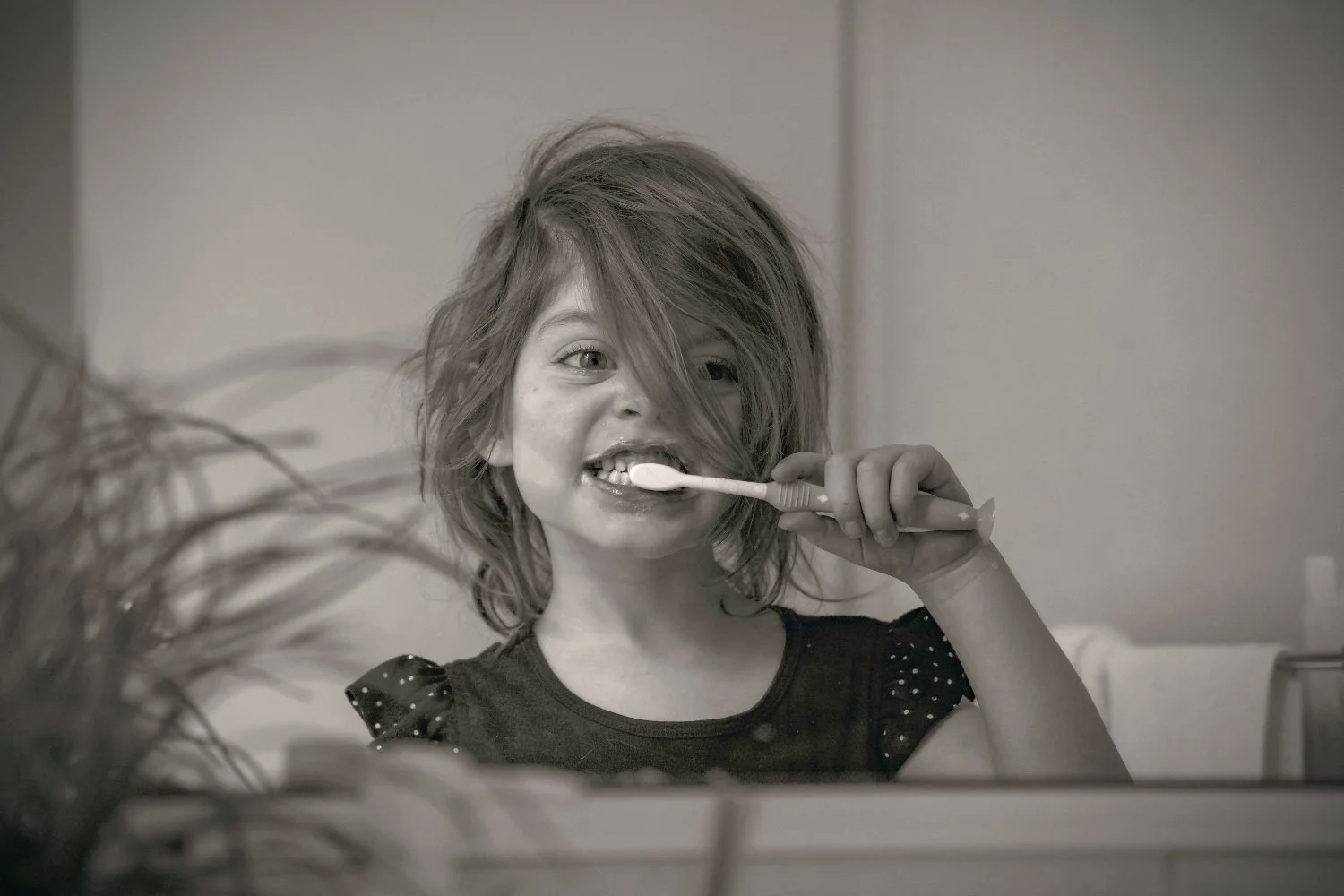 A girl with tousled hair brushes her teeth in the mirror