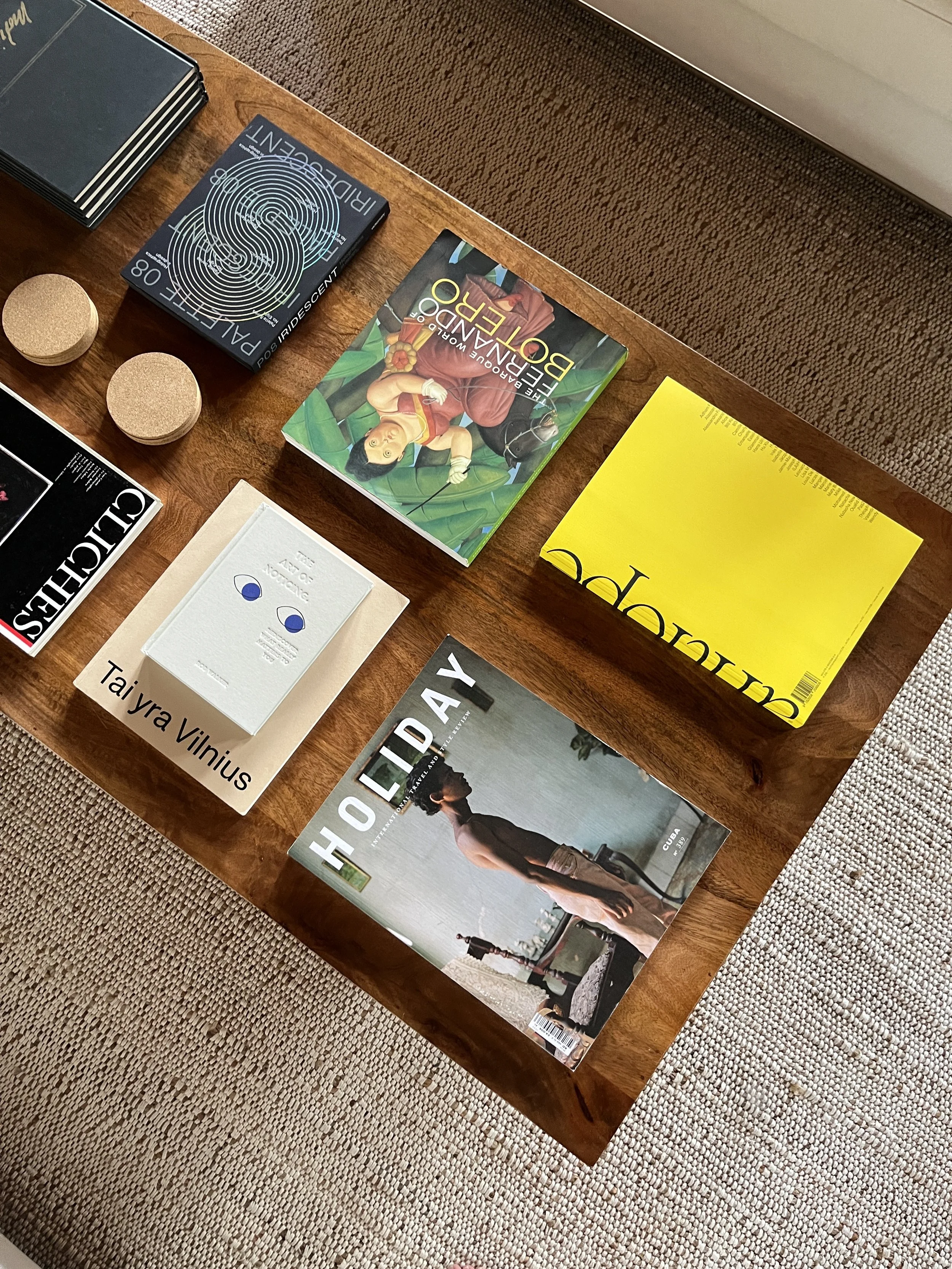 A styled wooden coffee table displaying curated design and art books, including “Holiday” and “Tai yra Vilnius,” arranged over a textured rug — showcasing creative inspiration and visual storytelling often used in interior design studios.