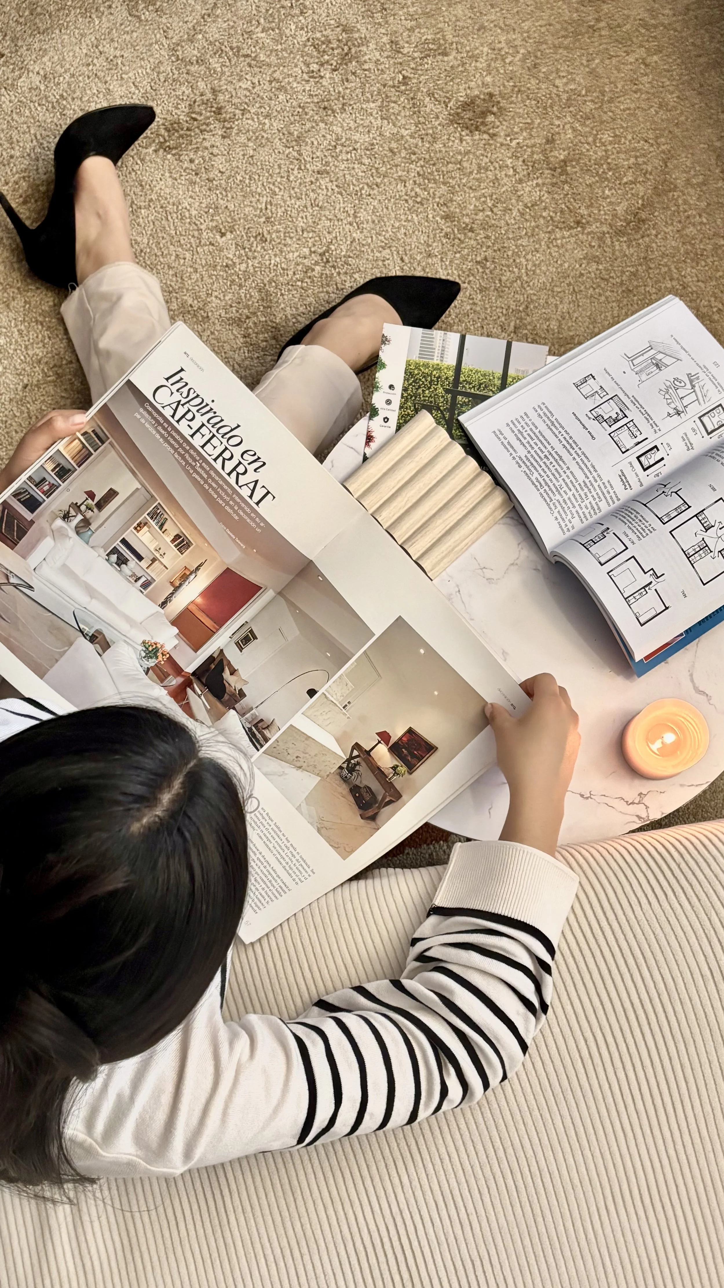 Cluttered creative desk with tea, magazines, AirPods and laptop, real life work from home interior designer business setup