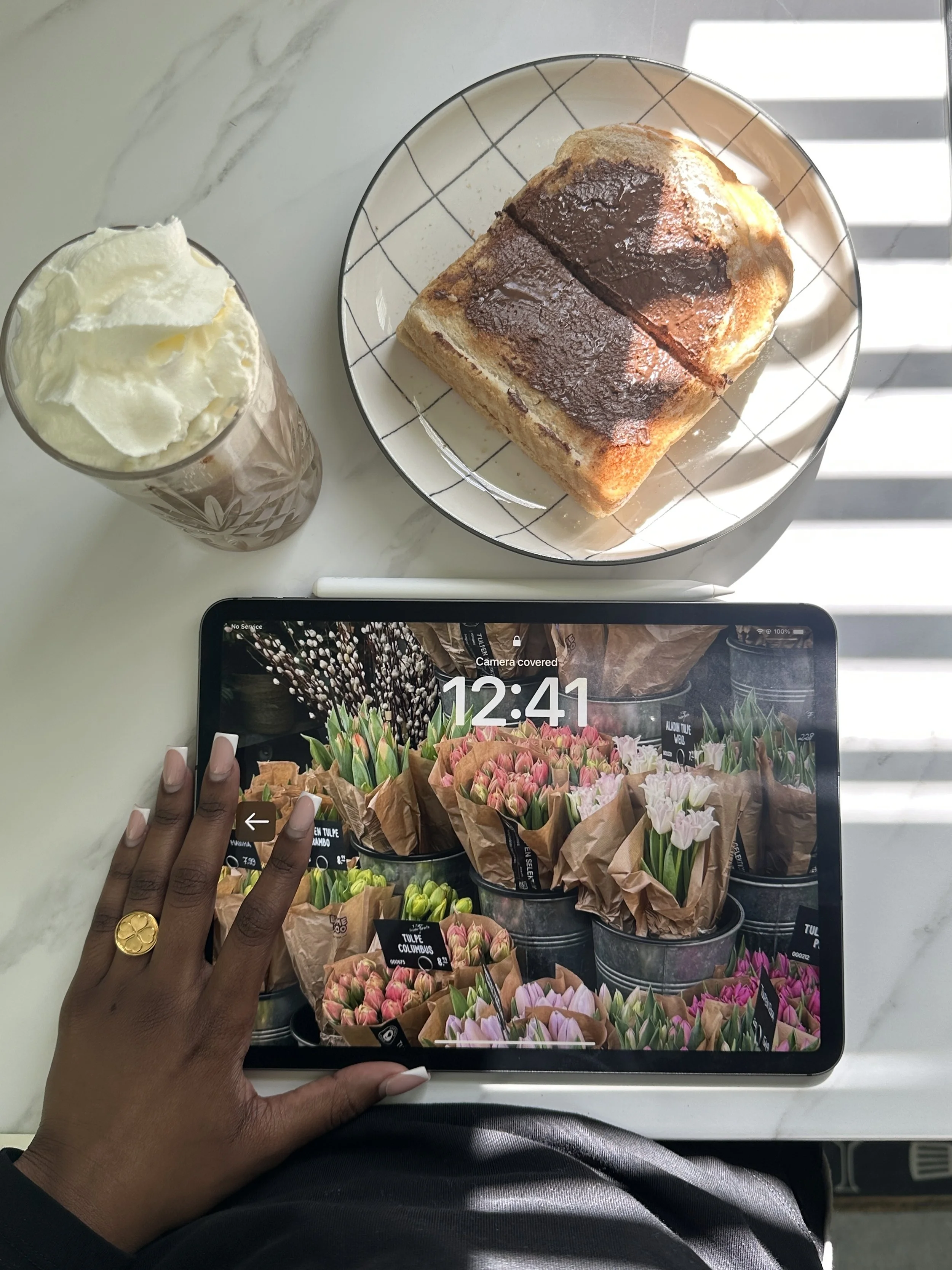 Hand holding iPad at marble table with iced coffee and toast, relaxed morning work session for interior design business marketing