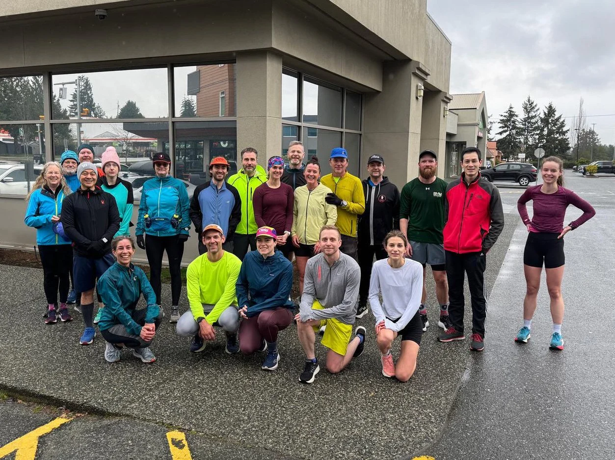 Group of people in athletic clothing posing outside a storefront on a rainy day.