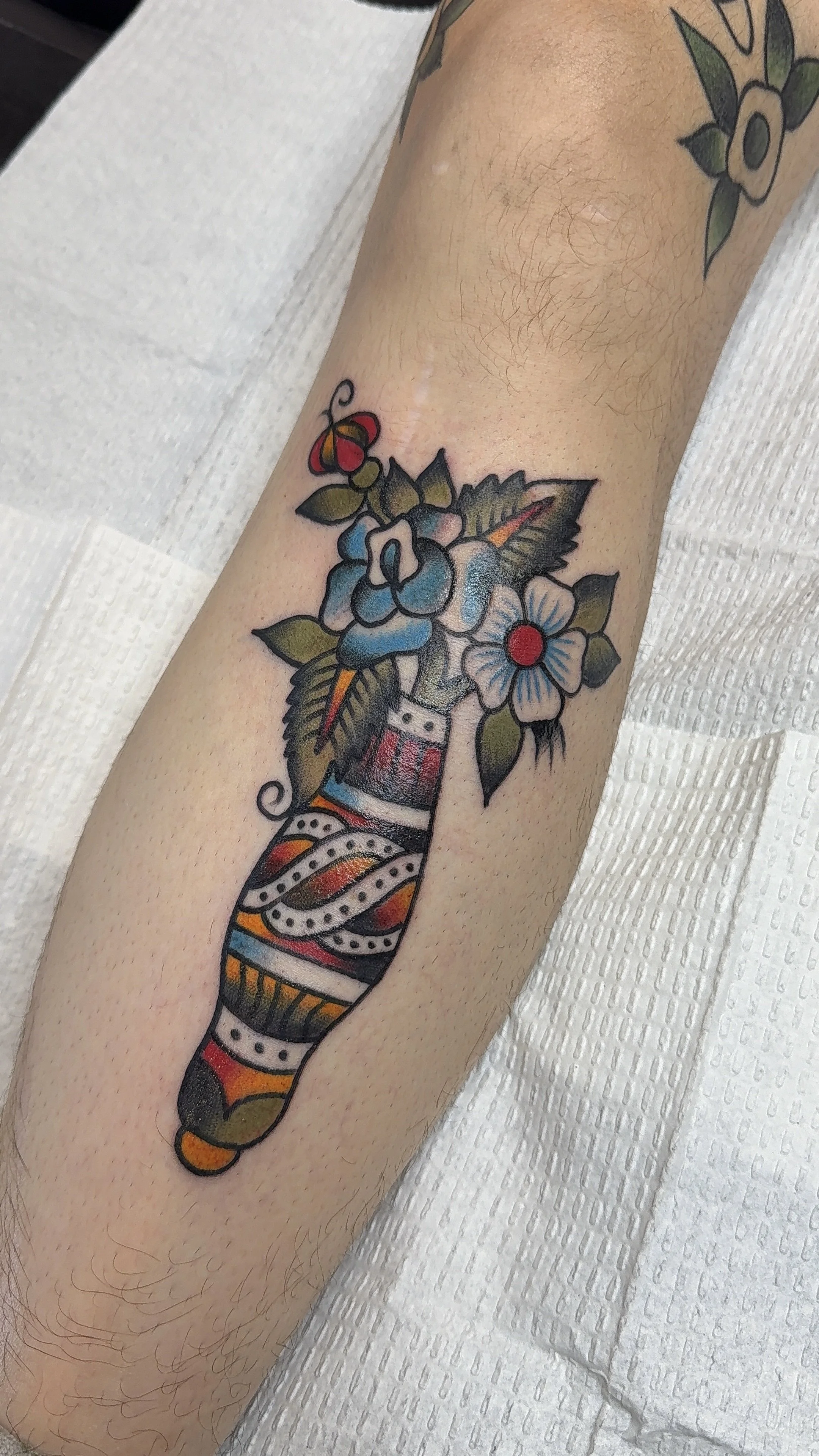 Colorful tattoo of a handgun with flowers and a butterfly on a person's arm.