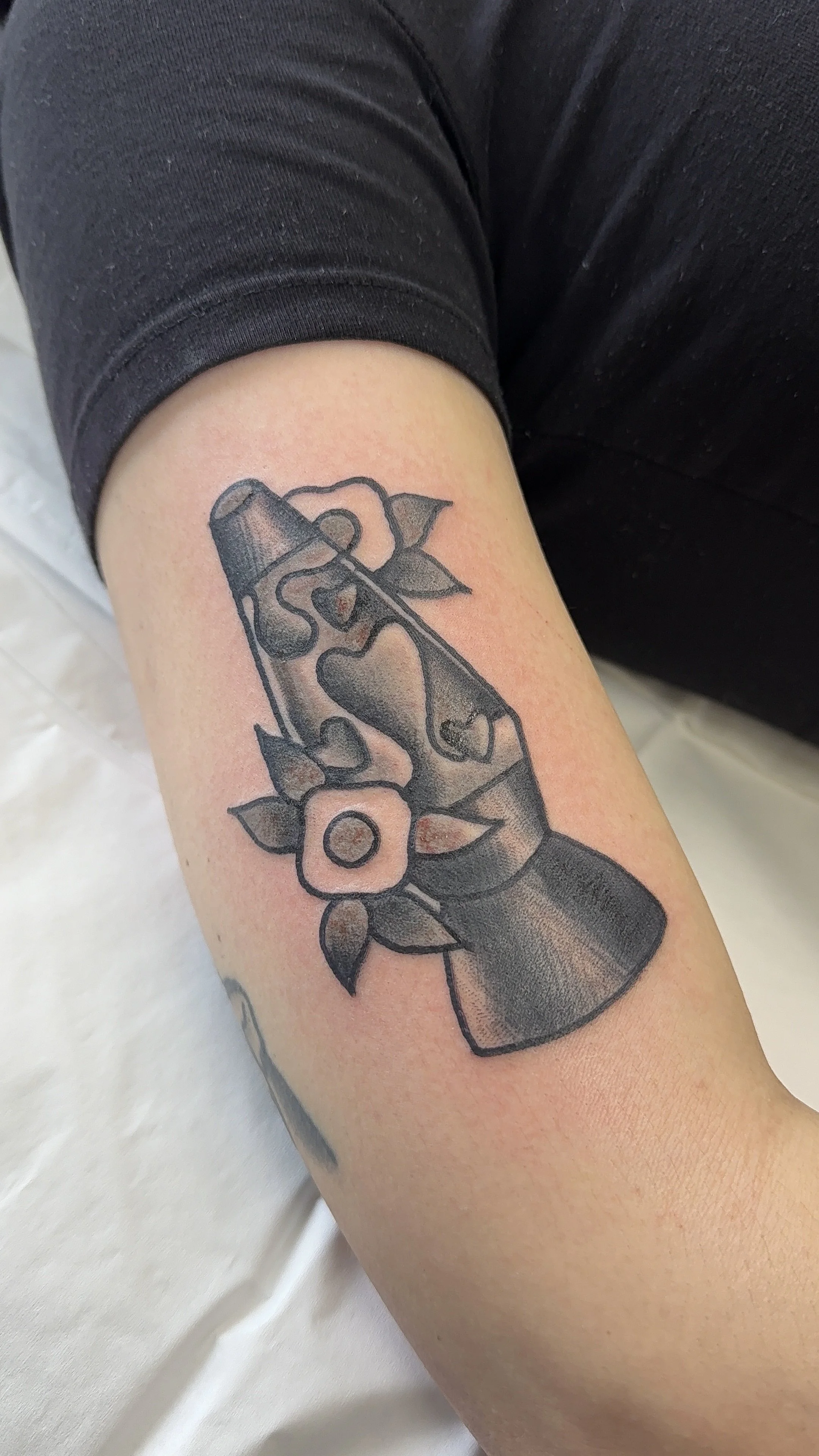 Black and gray tattoo of a lava lamp with a flower and leaves on a person's arm.