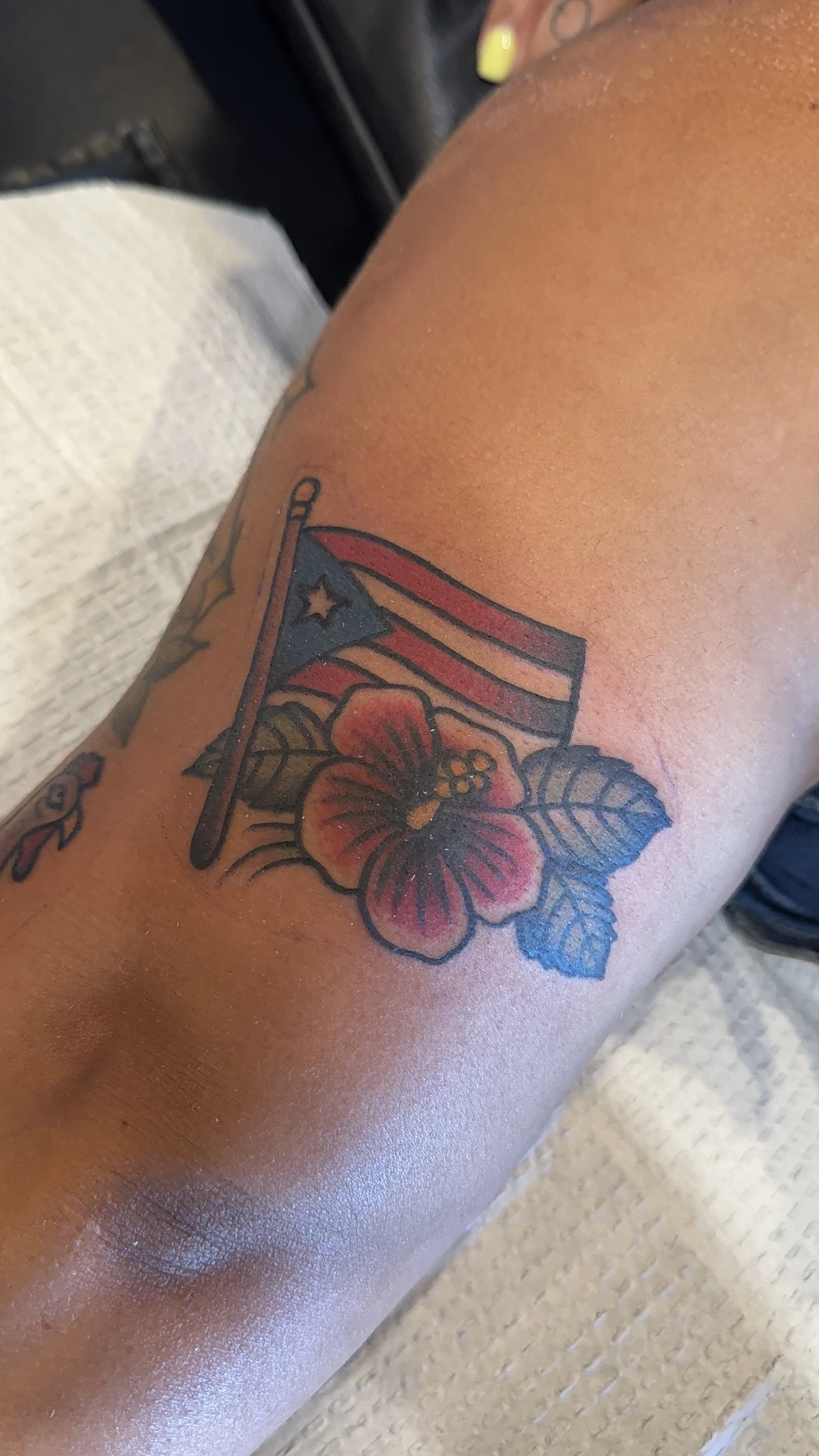 Tattoo of a Cuban flag with red, white, and blue colors, accompanied by a hibiscus flower with red petals and green leaves on a person's arm.