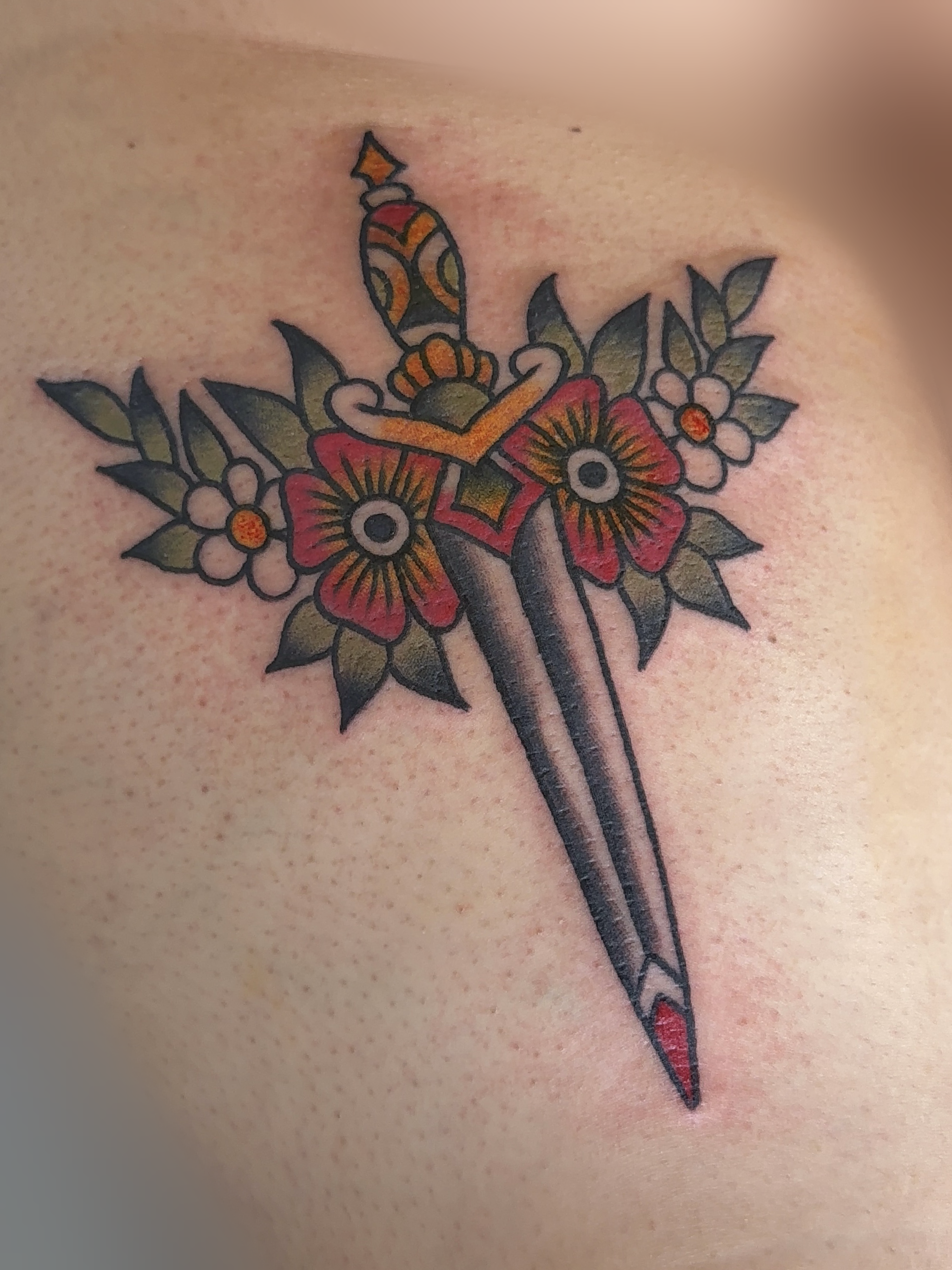 Tattoo of an American traditional style dagger with floral elements, including red flowers and green leaves.