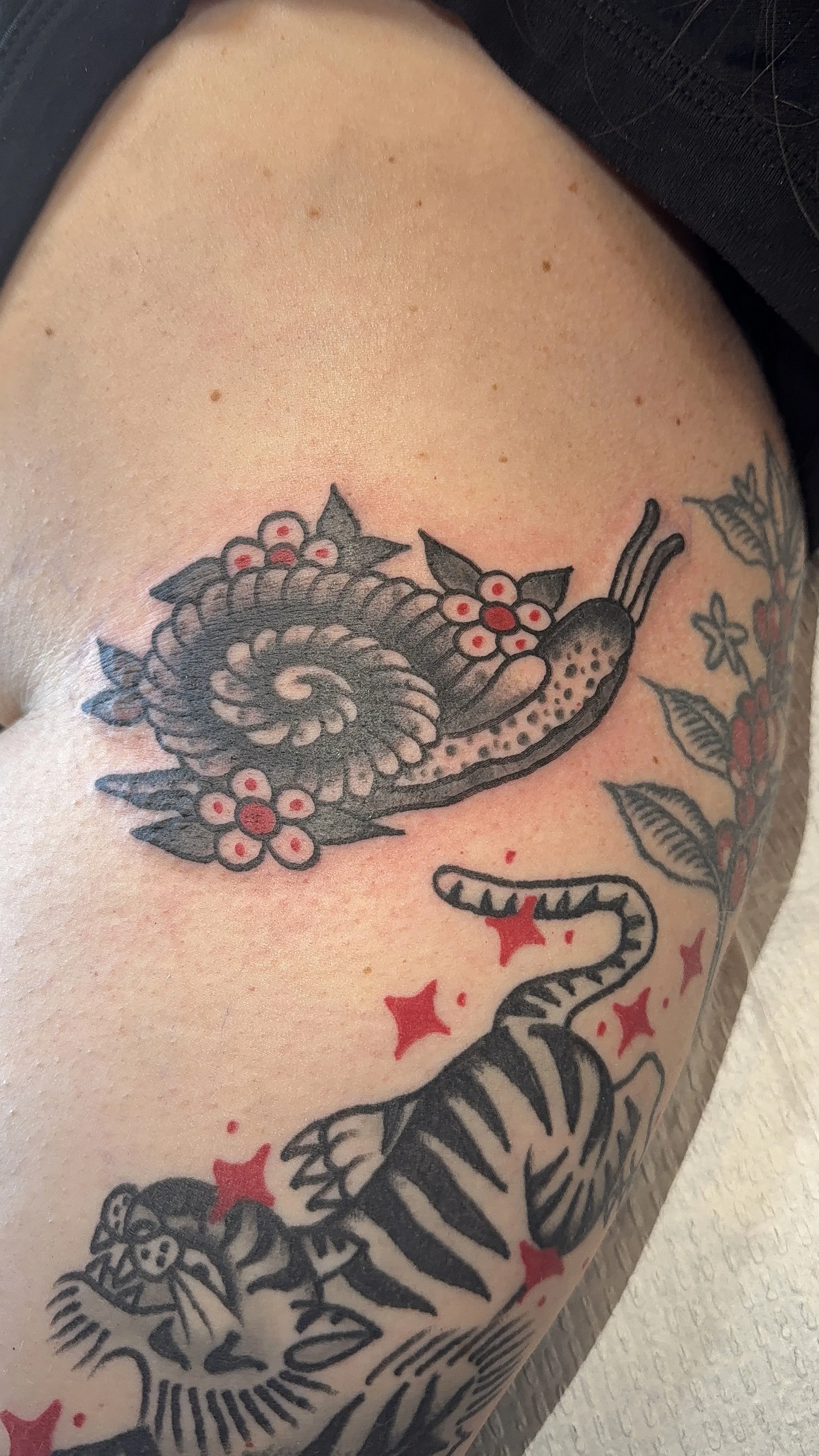 Tattoo of a snail with flowers and leaves on a person's upper arm or shoulder.