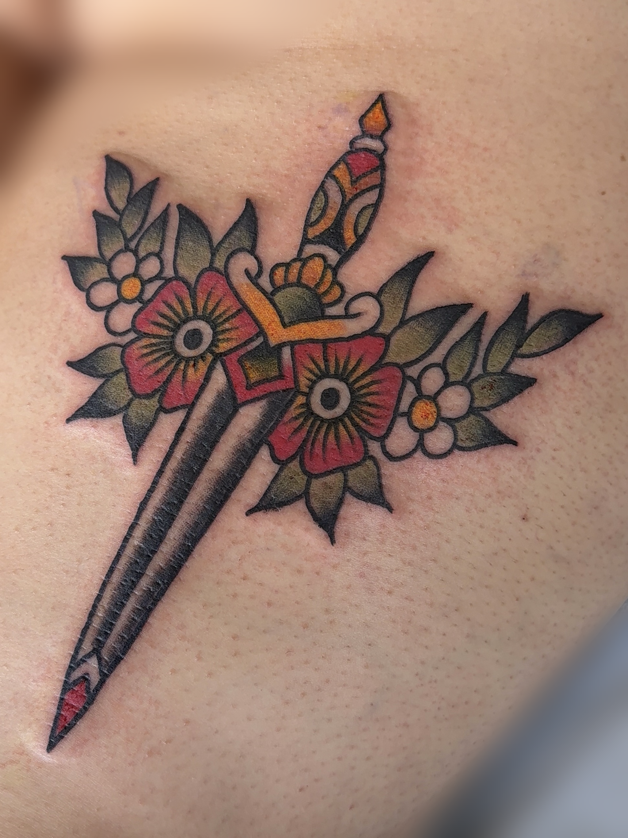 Close-up of a colorful floral tattoo with black outlines on skin.
