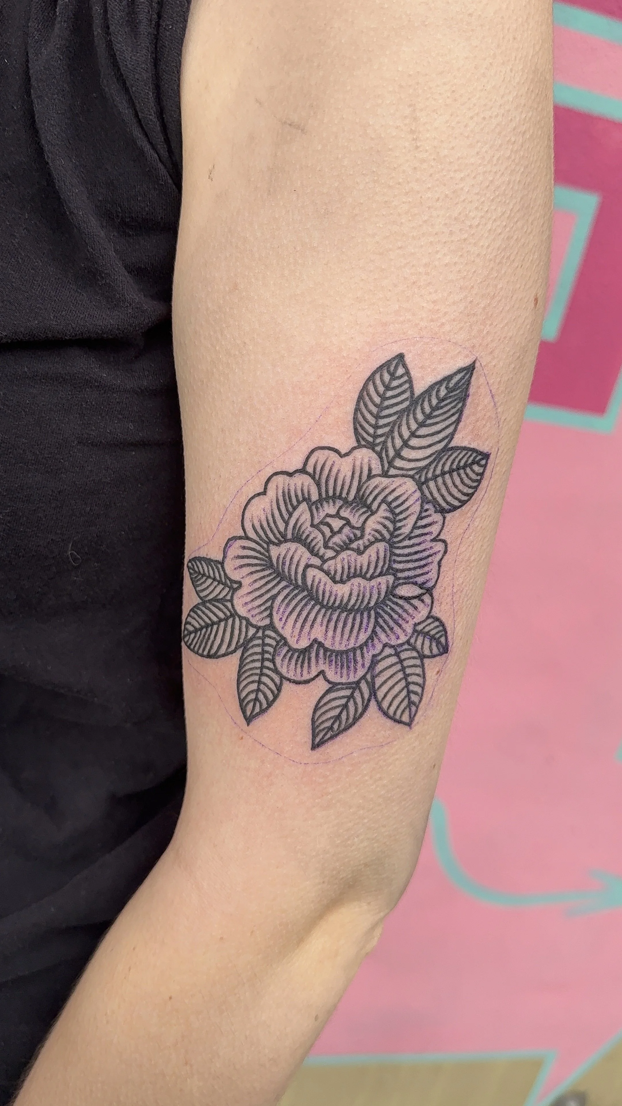 Black ink floral tattoo of a large, detailed peony with leaves on a person's inner arm.