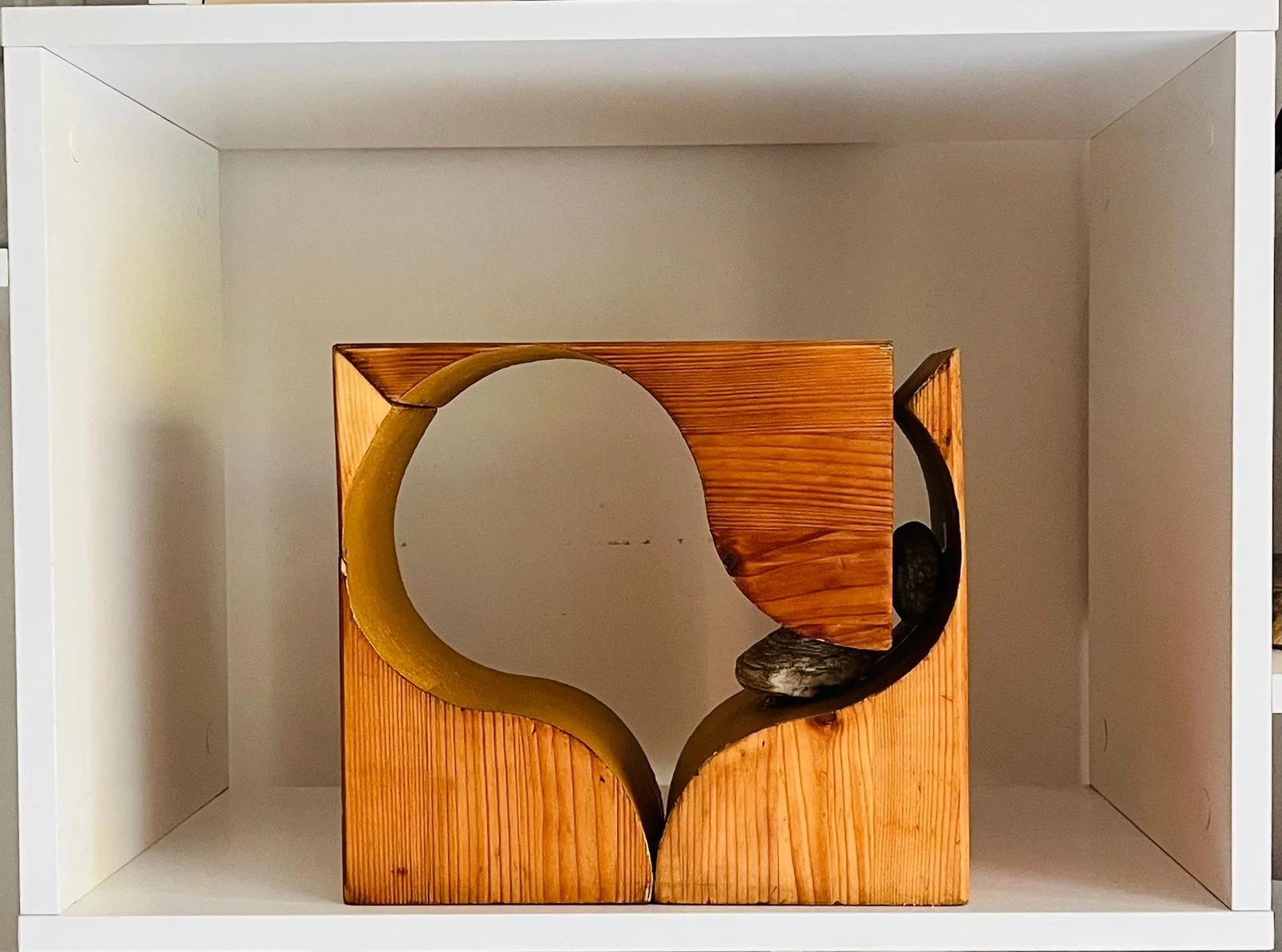 Wooden bookshelf with a circular cutout design, containing decorative stones inside, set within a white cabinet.