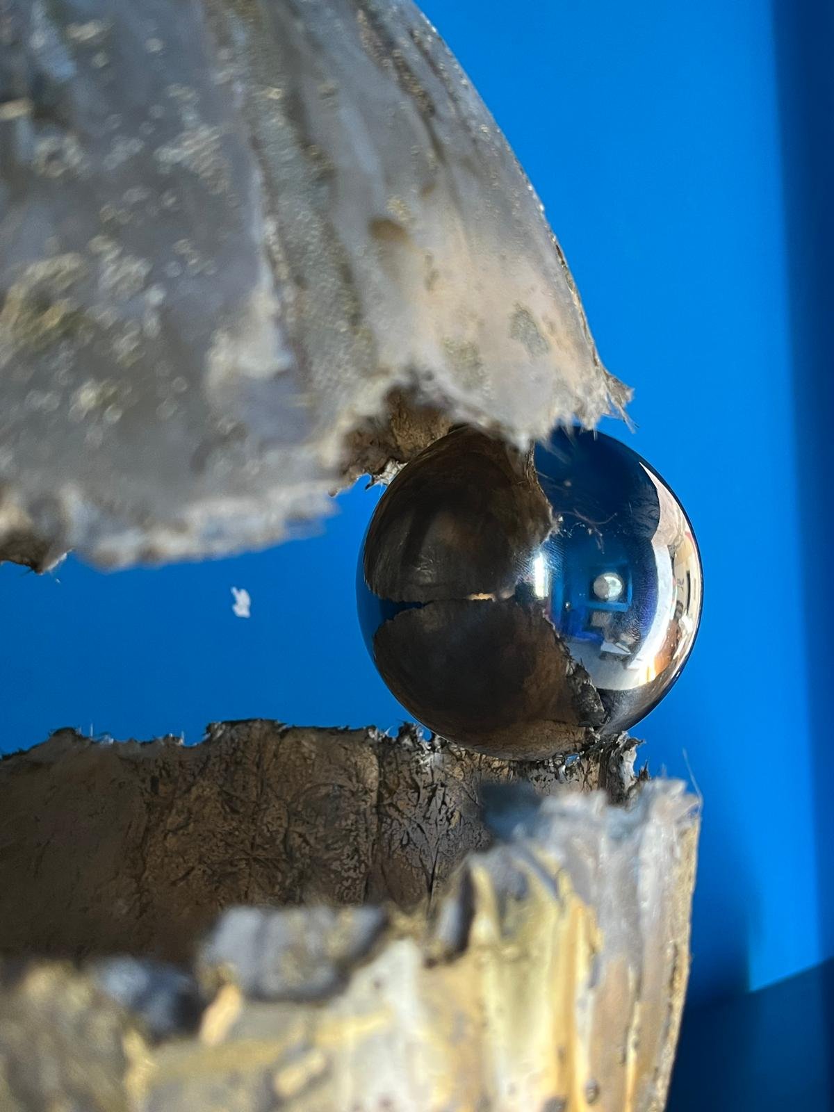 Close-up of a shiny metallic ball balanced on a rough, textured surface with torn edges, against a blue background.