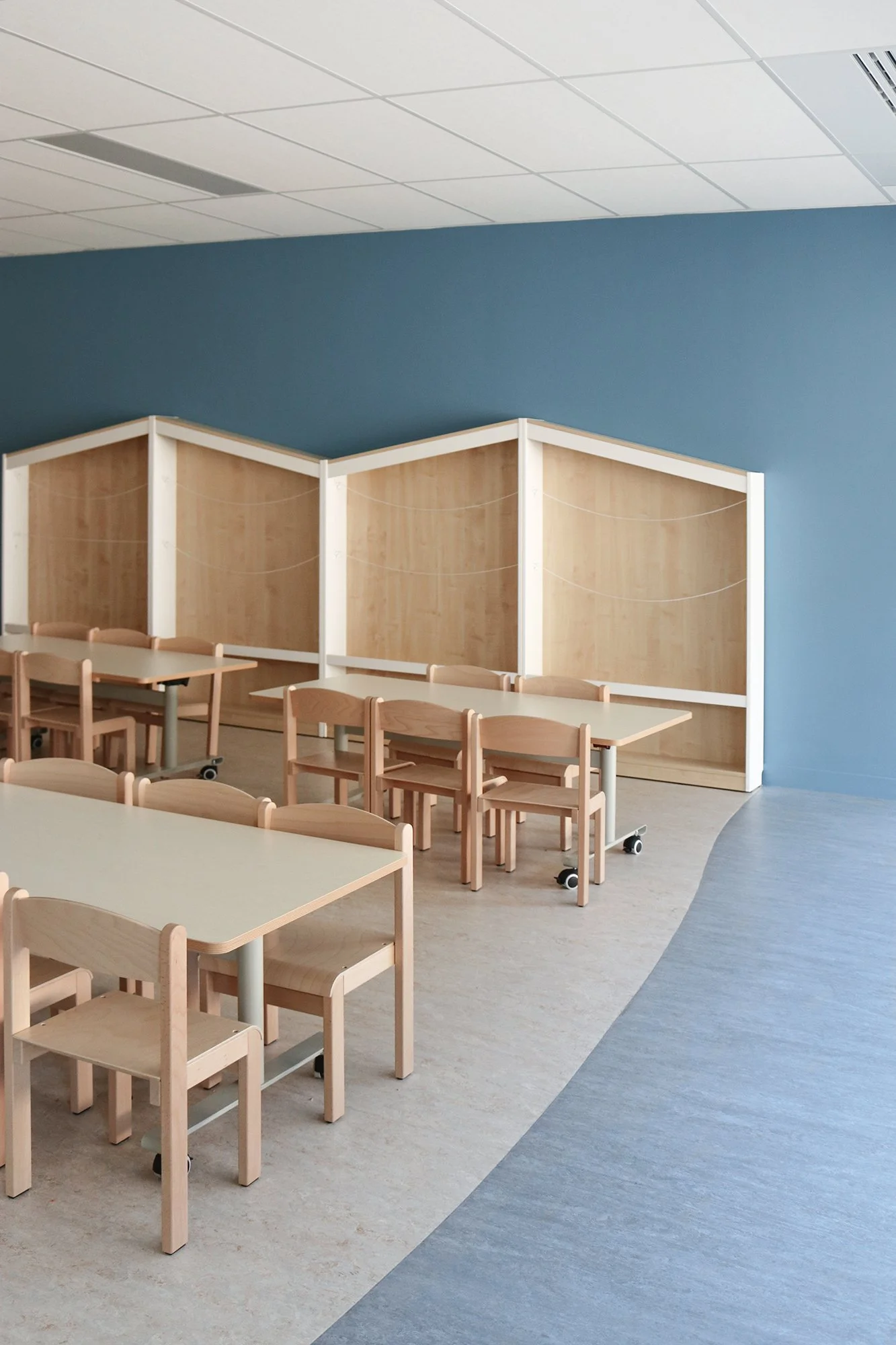 Salle d'activités calmes, mur bleu et mobilier  bois, espace périscolaire et RPE du Pôle enfance jeunesse de Champagne-au-mont-d'or