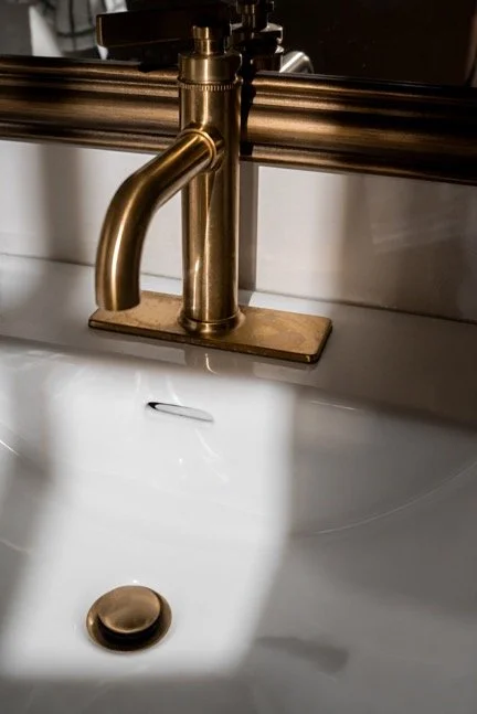 Arvoasunnossa kultainen tai pronssinen hana ja valkoinen posliiniallas.