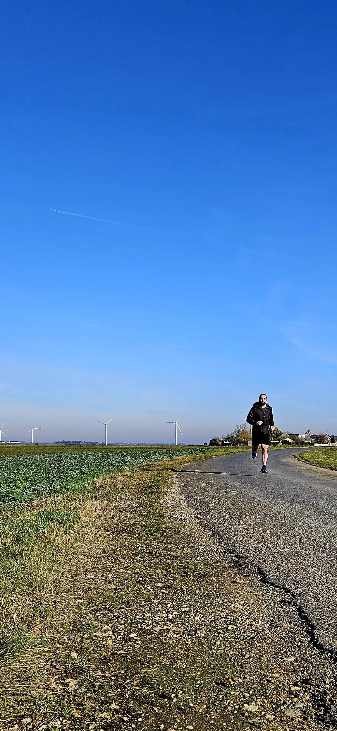 Person jogging on a rural road with wind turbines in the background under a clear blue sky.