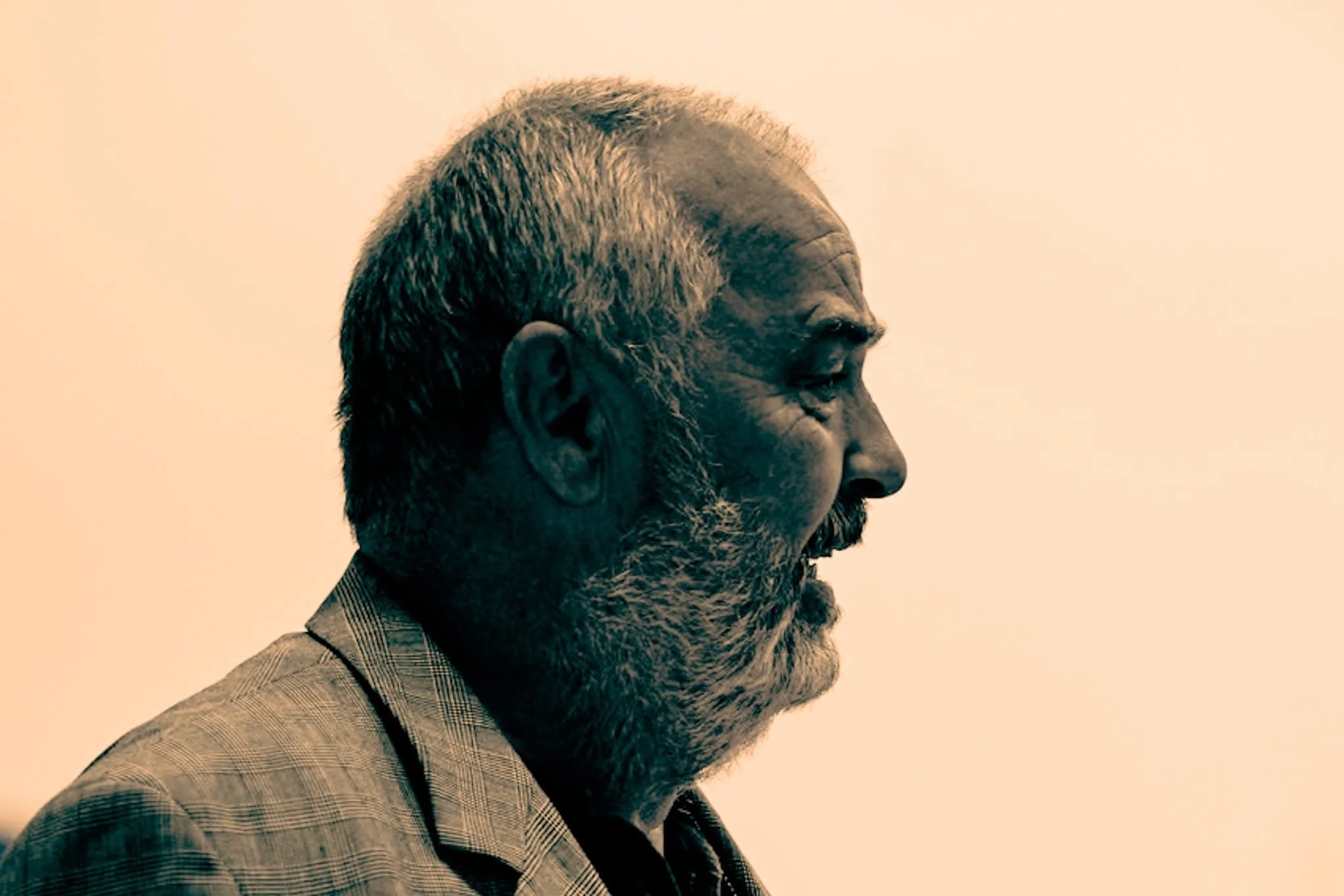 Side profile of a bearded man in a suit with sepia-toned lighting.