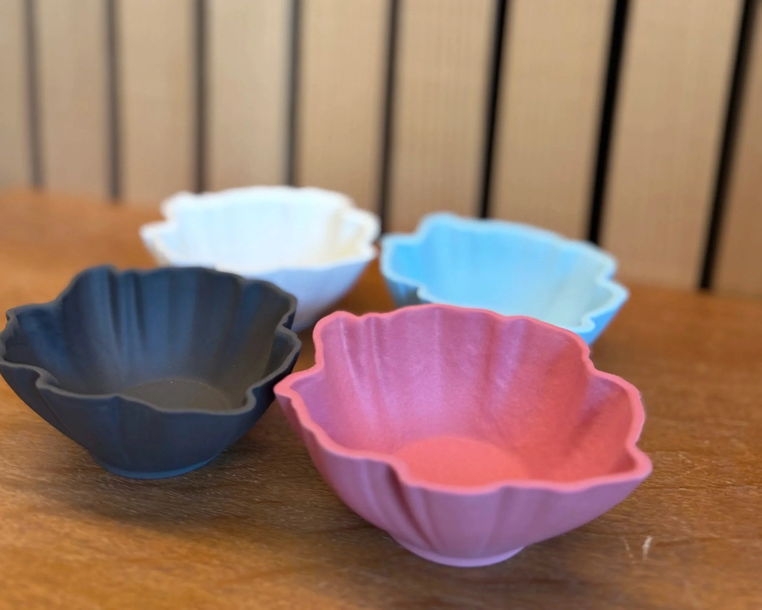 Fünf kleine bunte Schälchen in rosa, dunkelblau, hellblau, schwarz und cremefarben auf einem Holztisch.